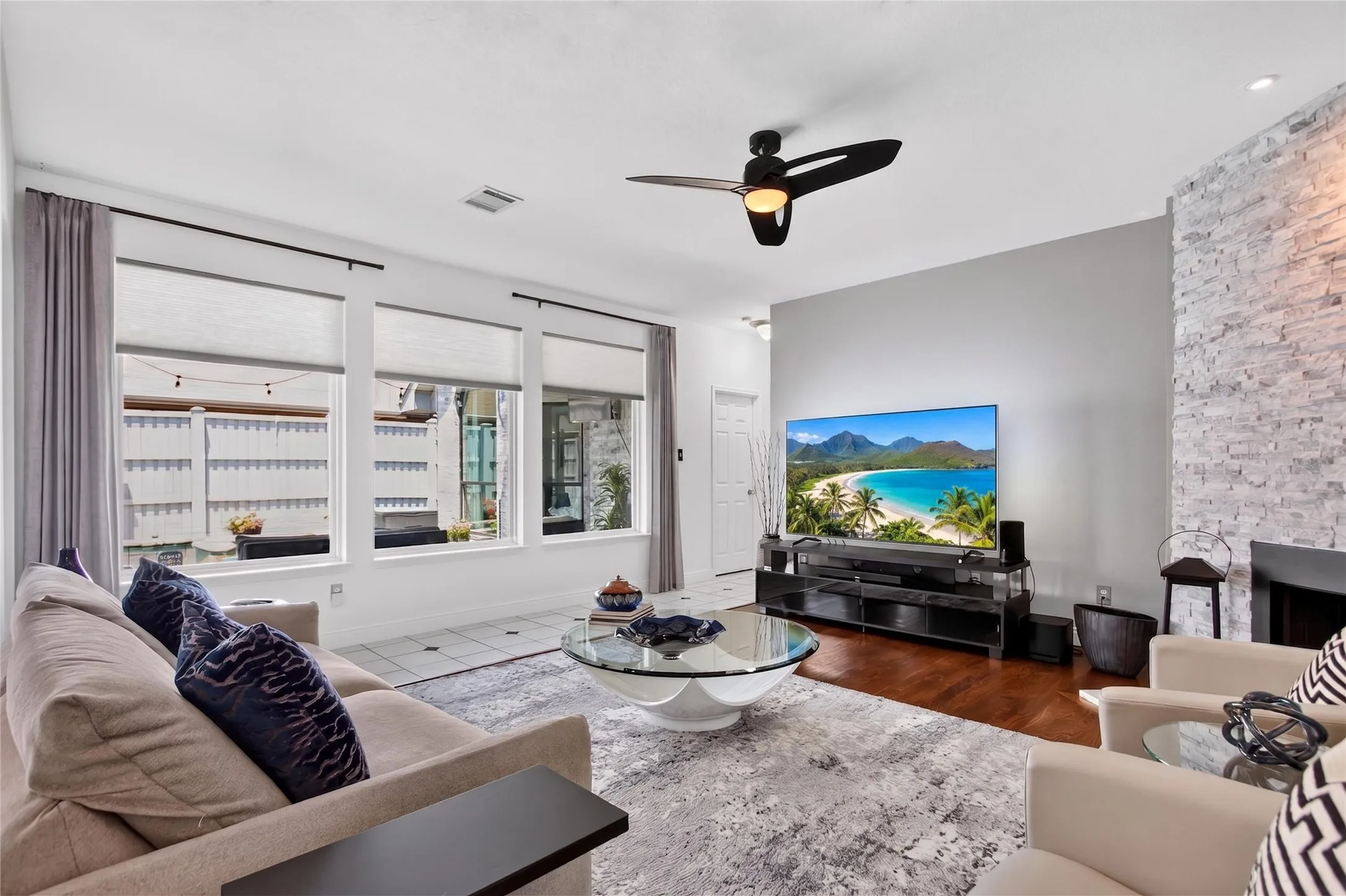 This spacious living room is filled with natural light from oversized vinyl windows and custom full window shades added in 2023.  Room has view of your private backyard oasis featuring a pool and spa and covered patio. A striking floor to ceiing gas fireplace serves as the room's dramatic focal point. Wood floors add to the warmth of your gathering space. 2022 All baseboards replaced.