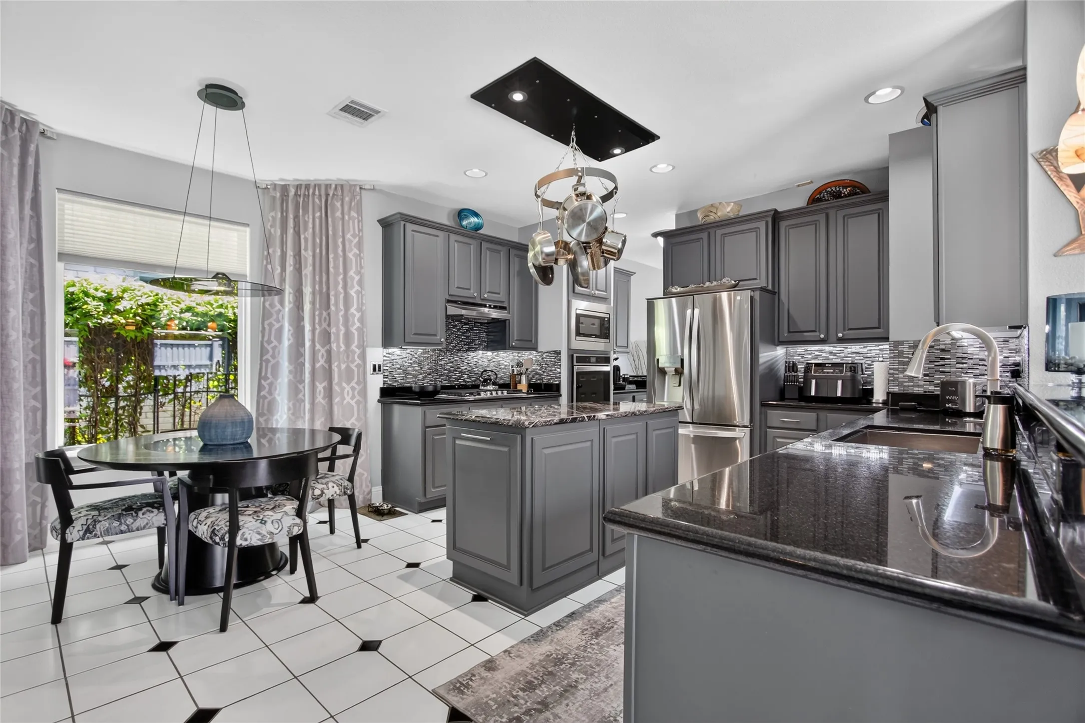 This beautifully appointed kitchen is designed to Impress, offering an expanded center island with a hidden trash pull-out bin, grantie counter tops, abundate work space, recessed lighting, under cabinet lighting, deep SS sink with updated faucet and durable tile floors. A reinforced ceiling mounted cookware rack adds both function and character.