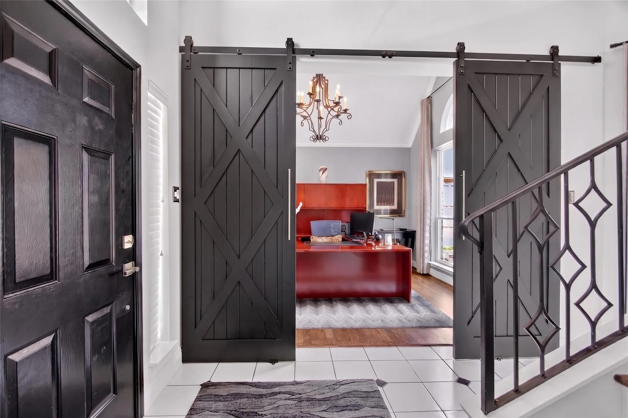Foyer with view of home office with elegant sliding wood doors. Staircase black balusters and designer light fixture  blend sophistication and warmth to welcome guests.