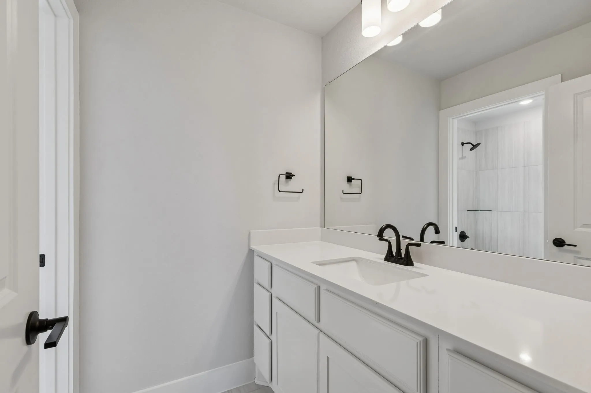 White vanity with integrated sink, white countertop, matte black hardware, and wall-mounted mirror