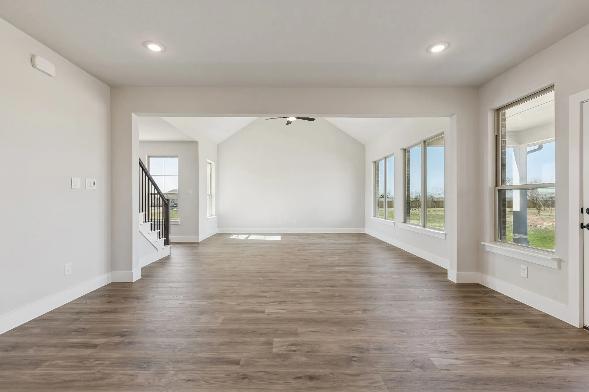 Spacious living area featuring wood-finish flooring, recessed lighting, expansive windows, and a vaulted ceiling