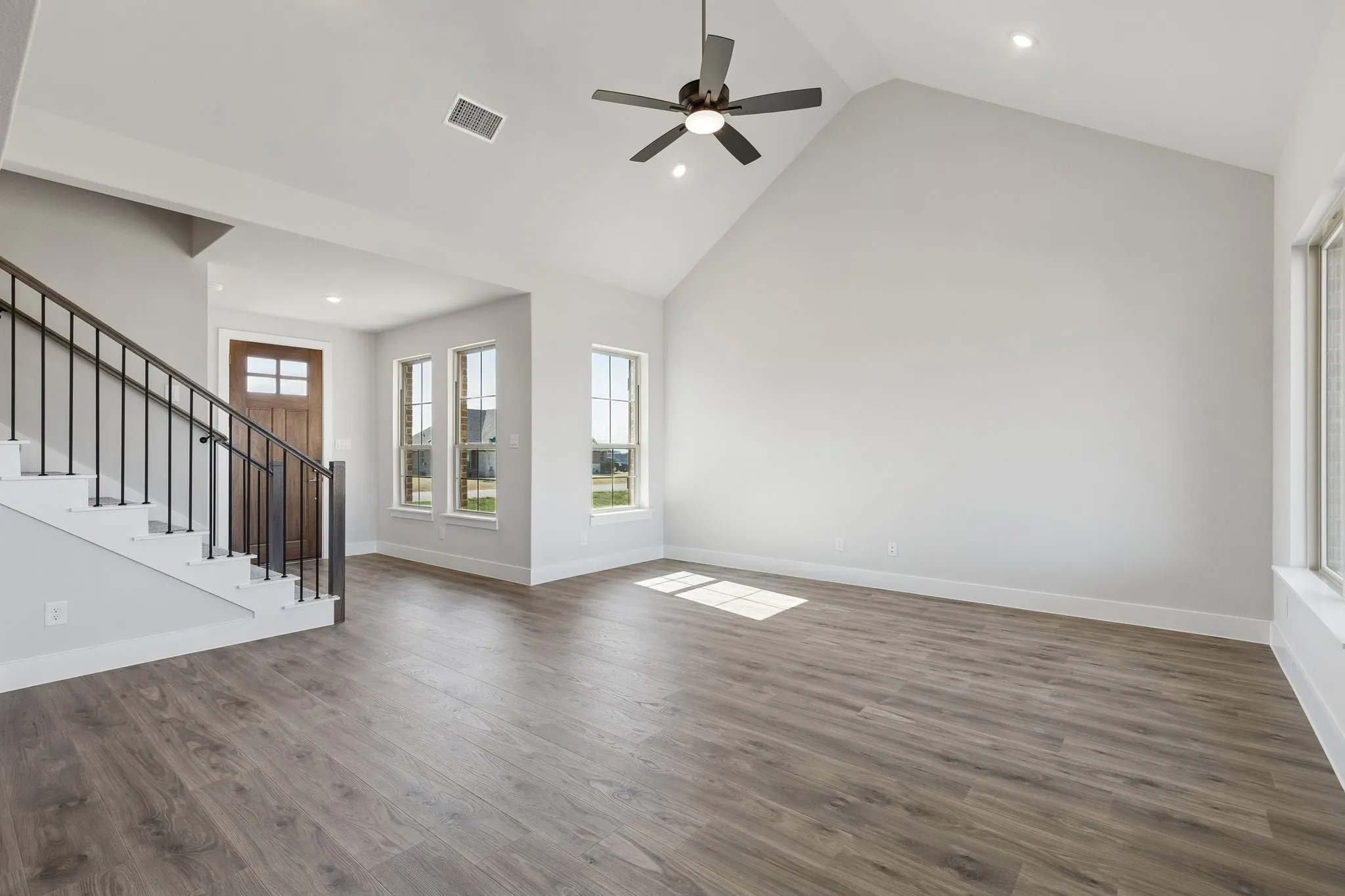 Vaulted ceiling with a ceiling fan, recessed lighting, wood-finish flooring, and multiple windows