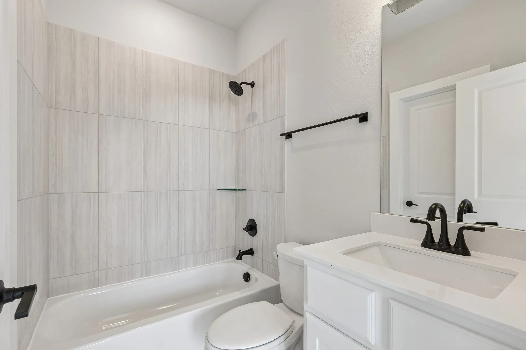 Shower-tub combination with tile surround, glass shelf, and matte black fixtures