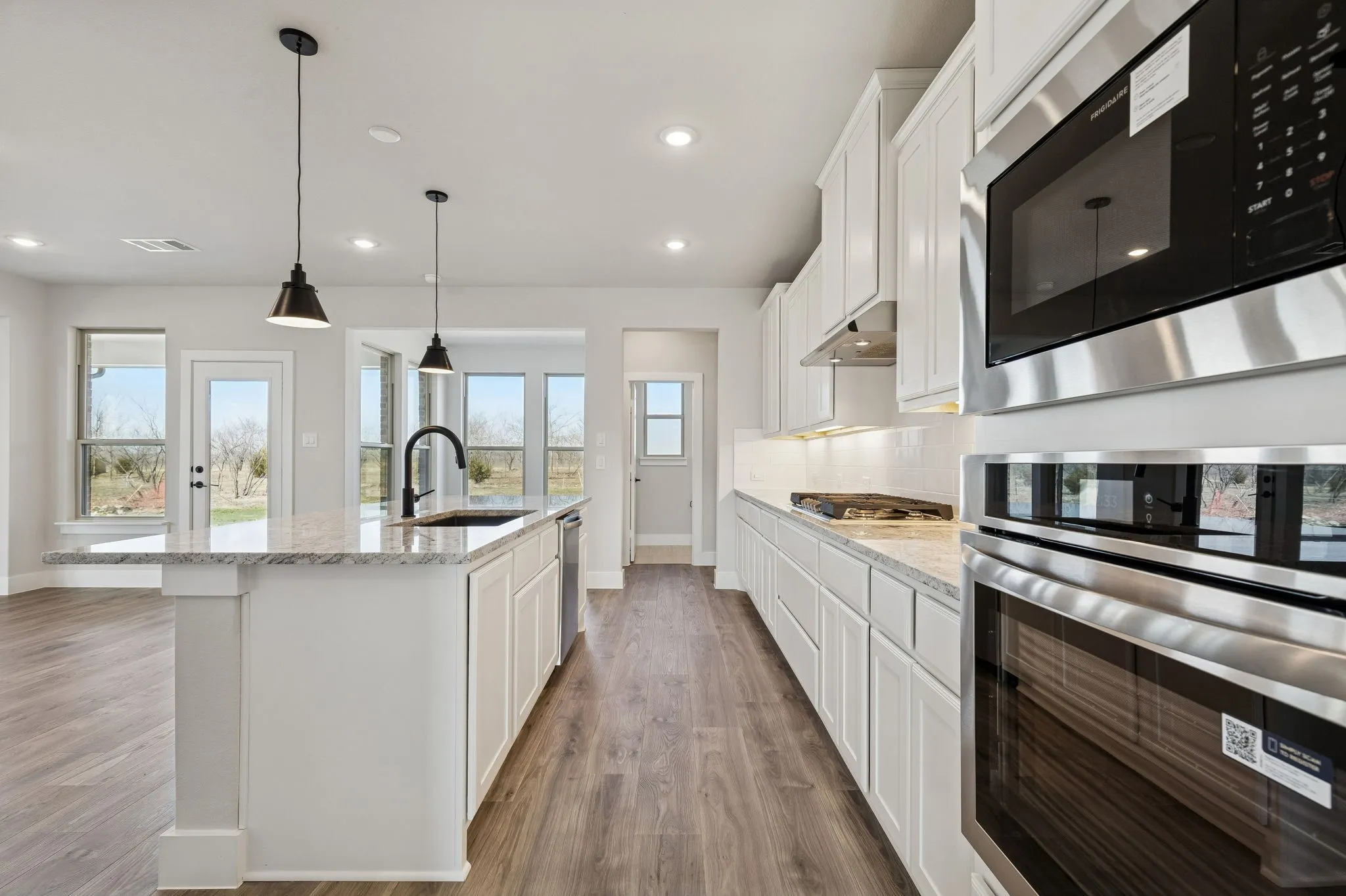 White cabinetry, stone countertops, stainless steel appliances, wood-finish flooring, and recessed lighting