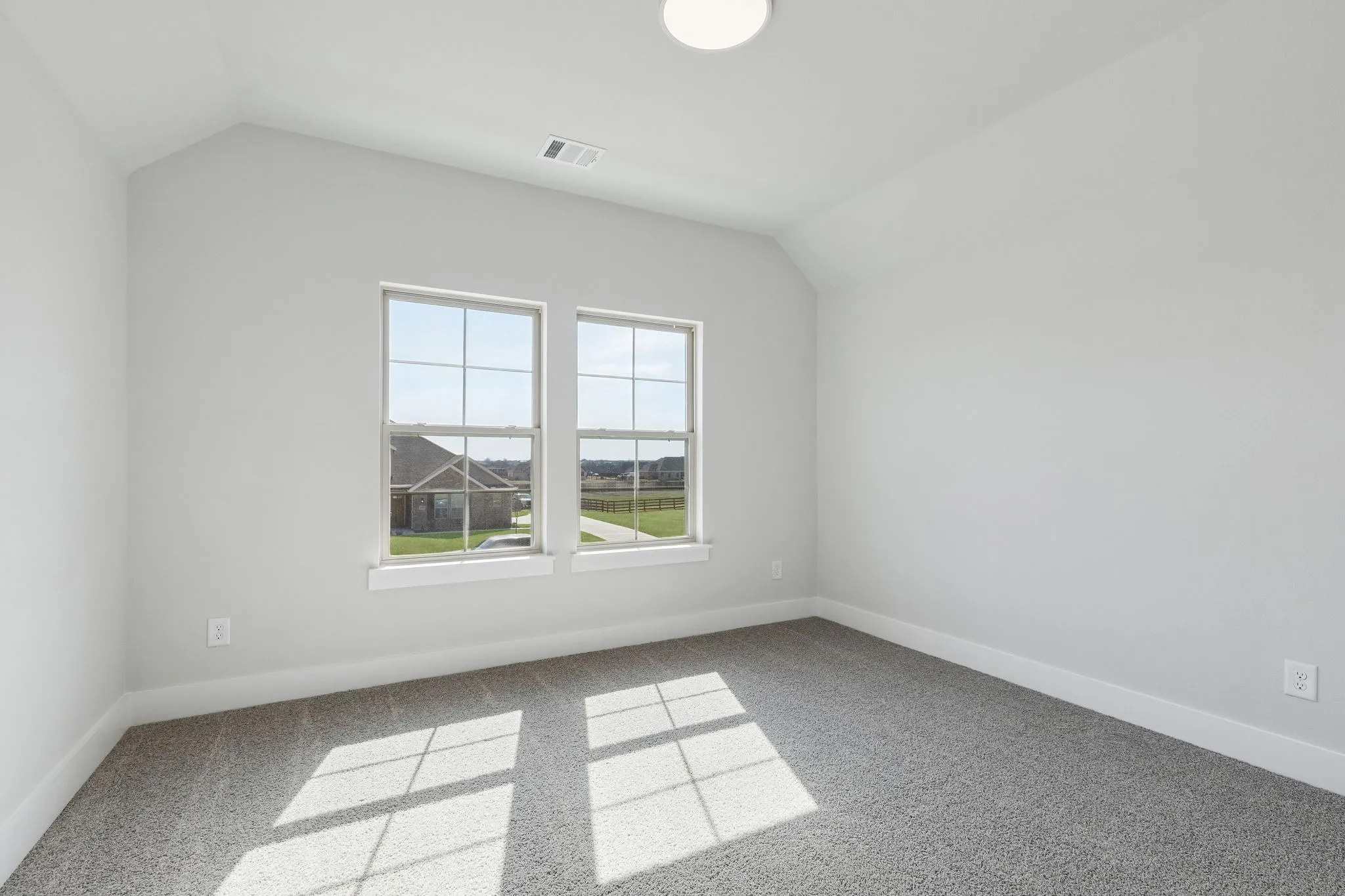 Vaulted ceiling, two windows with gridded panes, light gray carpet flooring, white trim, and a flush mount ceiling light