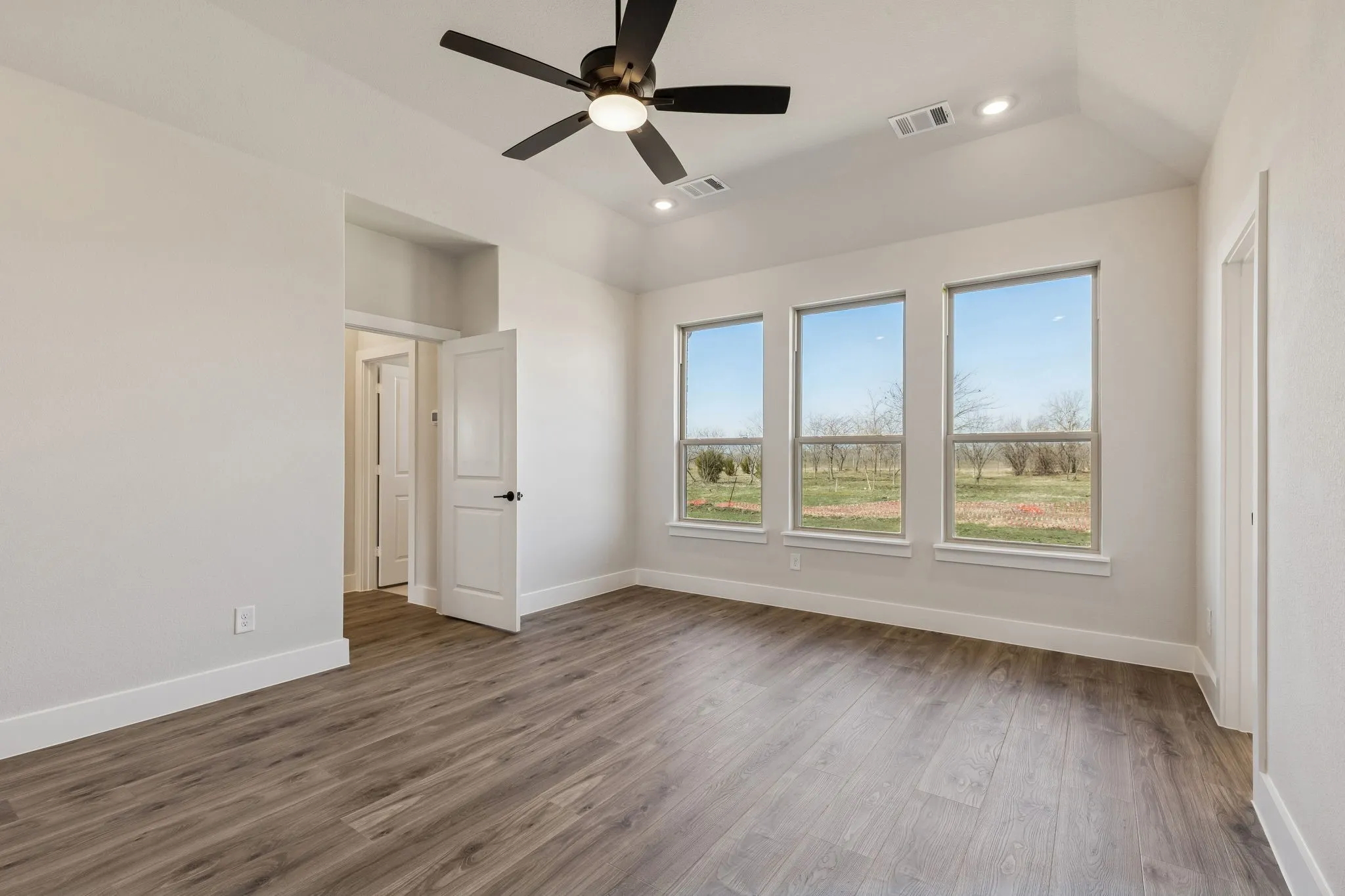 Wood-finish flooring, recessed lighting, ceiling fan, vaulted ceiling, and three large windows