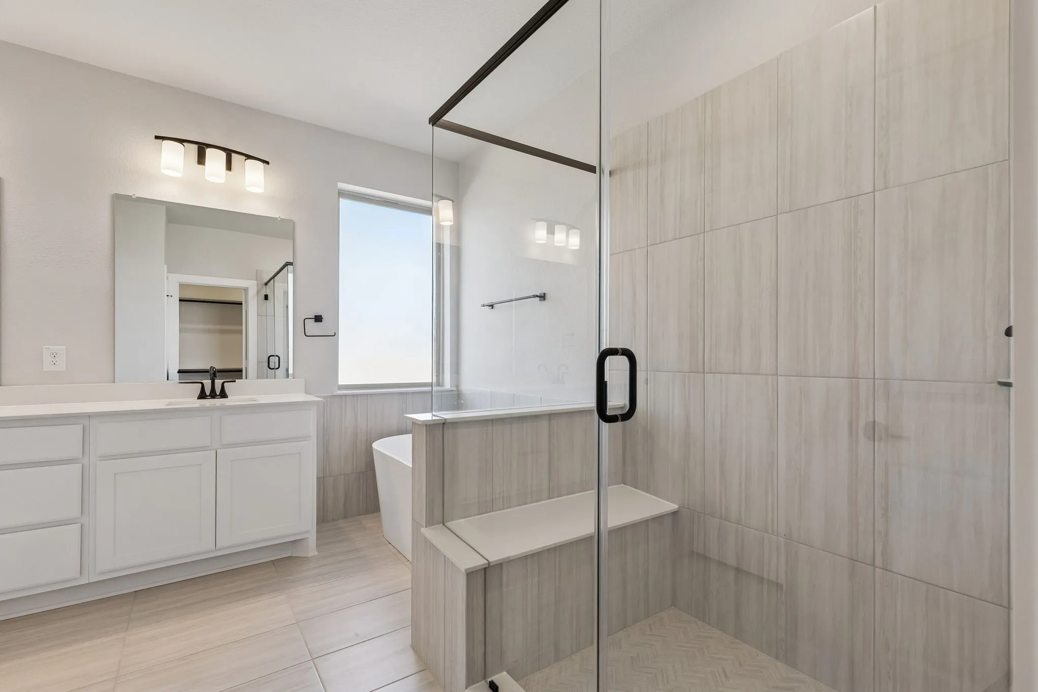 Spacious bathroom featuring a glass-enclosed shower with a built-in bench, a separate soaking tub, and a vanity with dual sinks