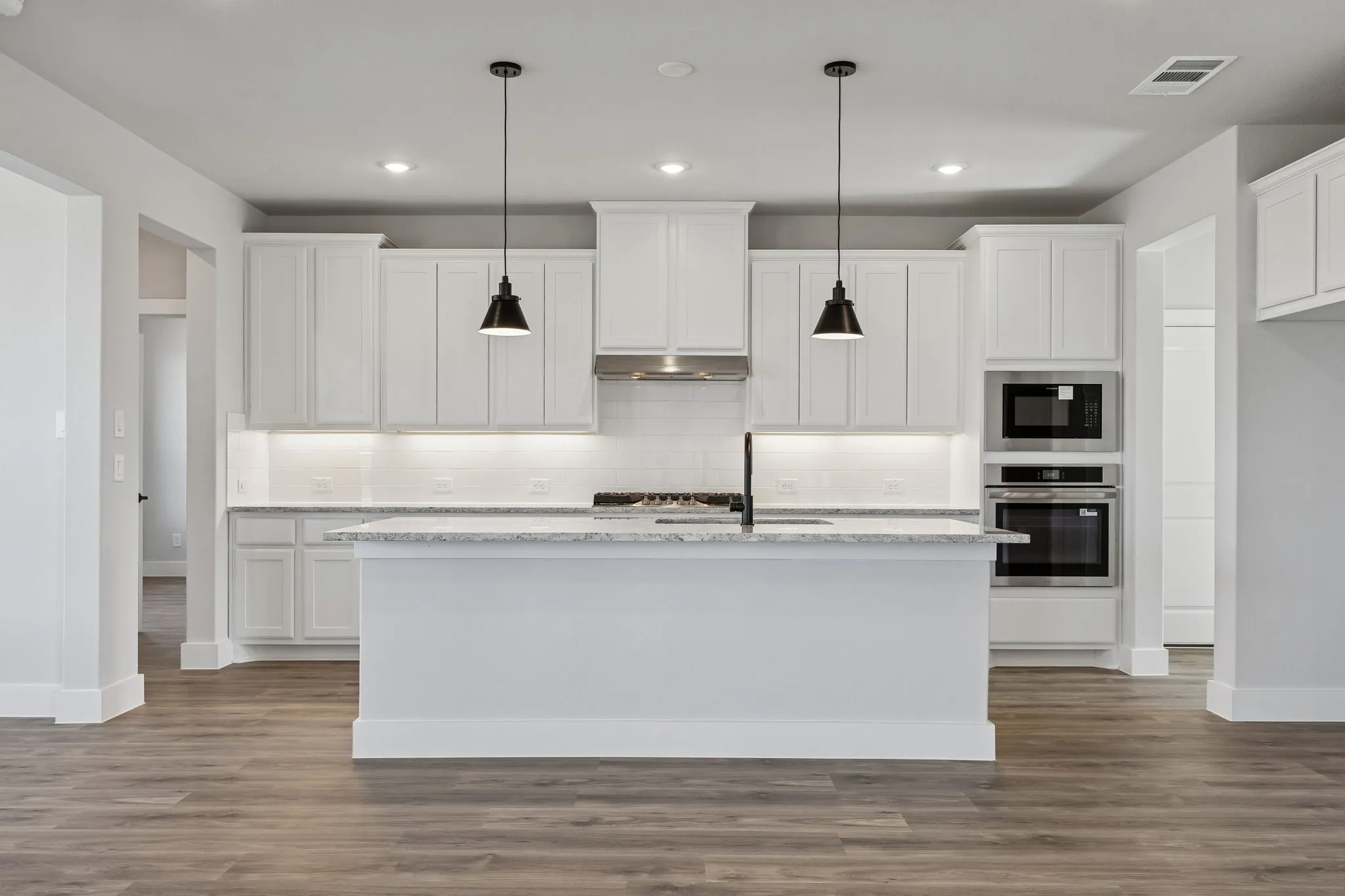Kitchen featuring white cabinetry, a central island with a sink, stainless steel appliances, and wood-finish flooring