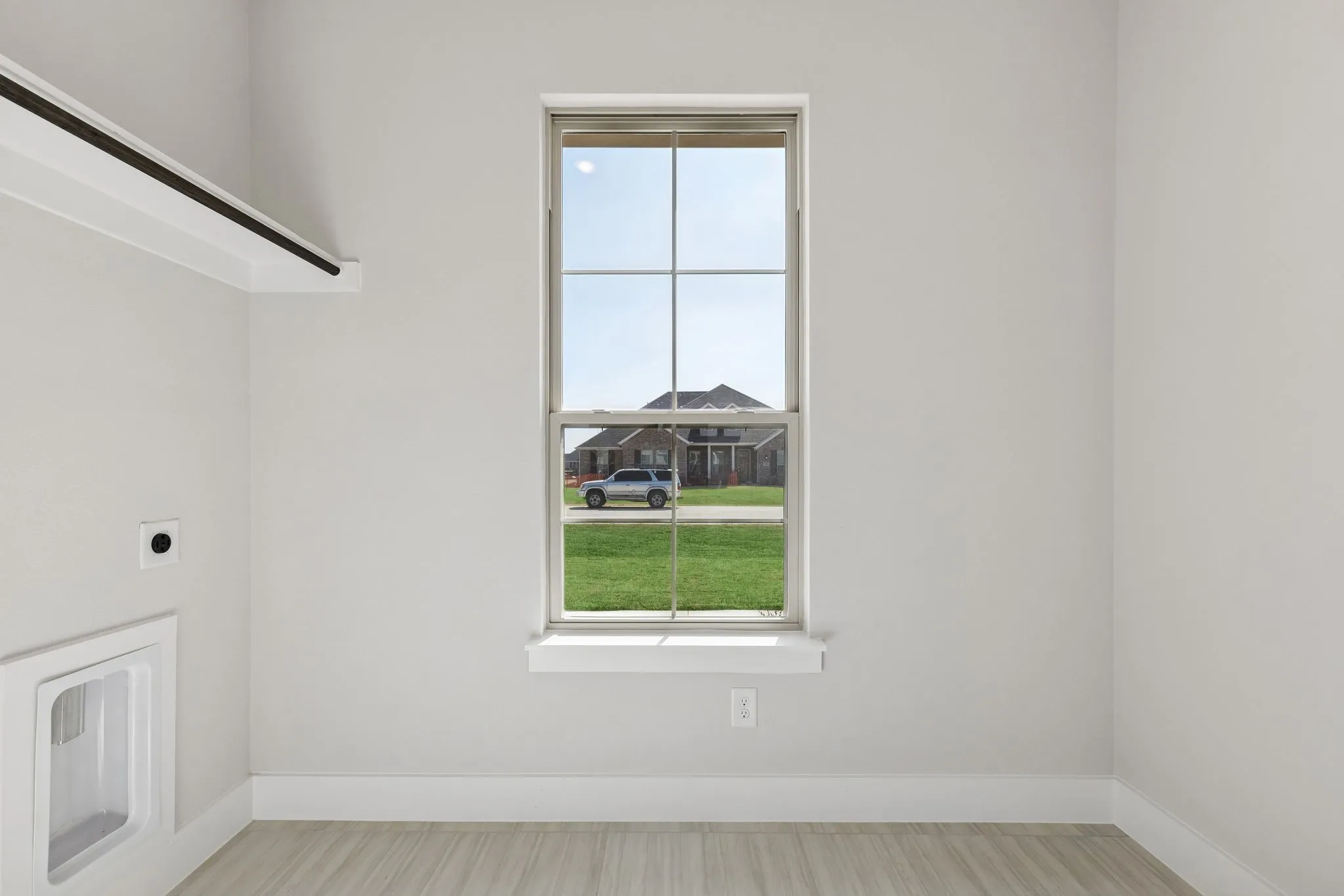 Single-hung window, light wood-finish flooring, white wall paint, wall-mounted drying rack, and built-in washing machine utility box