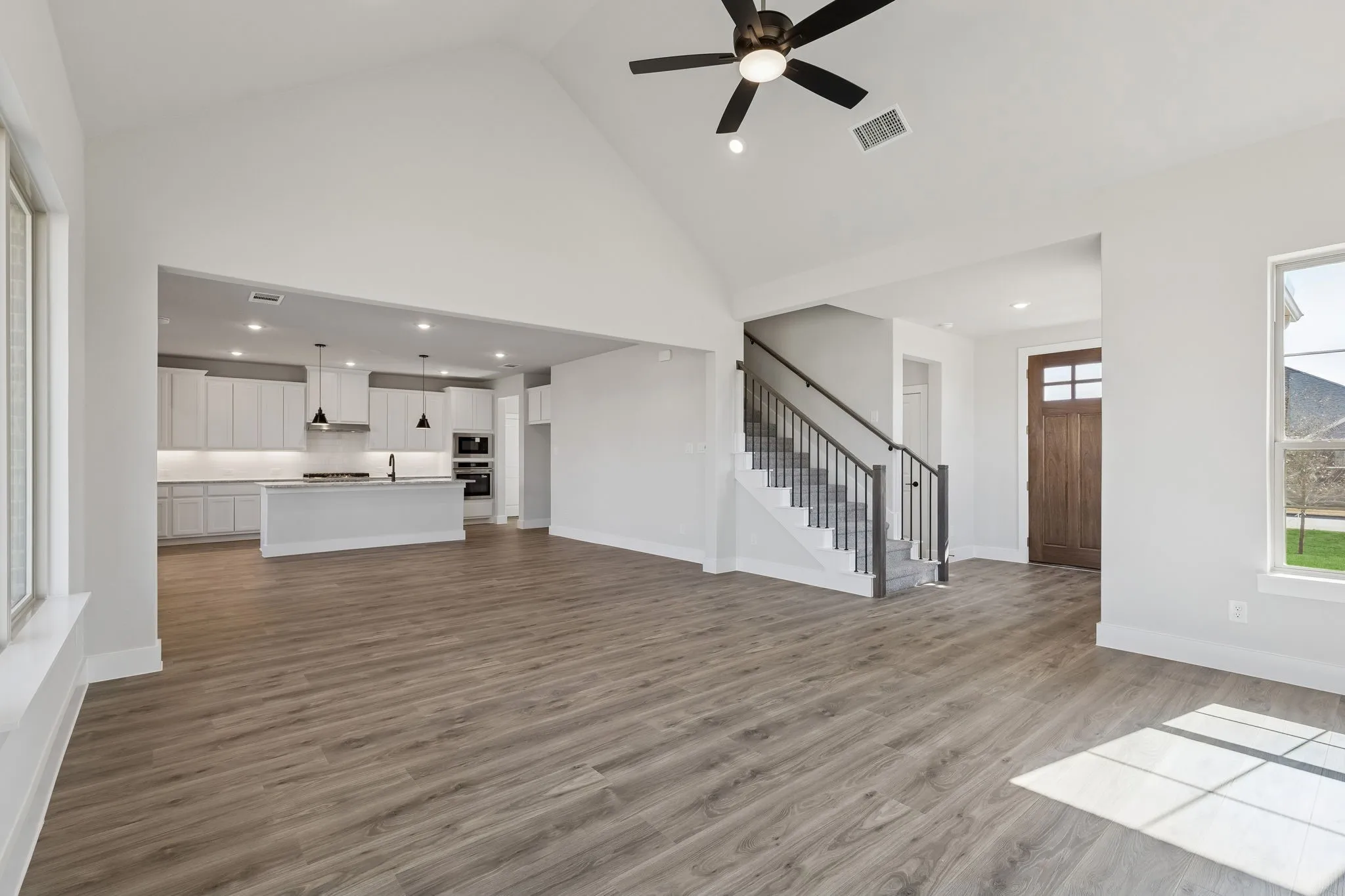Vaulted ceiling, wood-finish flooring, staircase with metal balusters, kitchen with pendant lighting and built-in appliances, and a paneled entry door