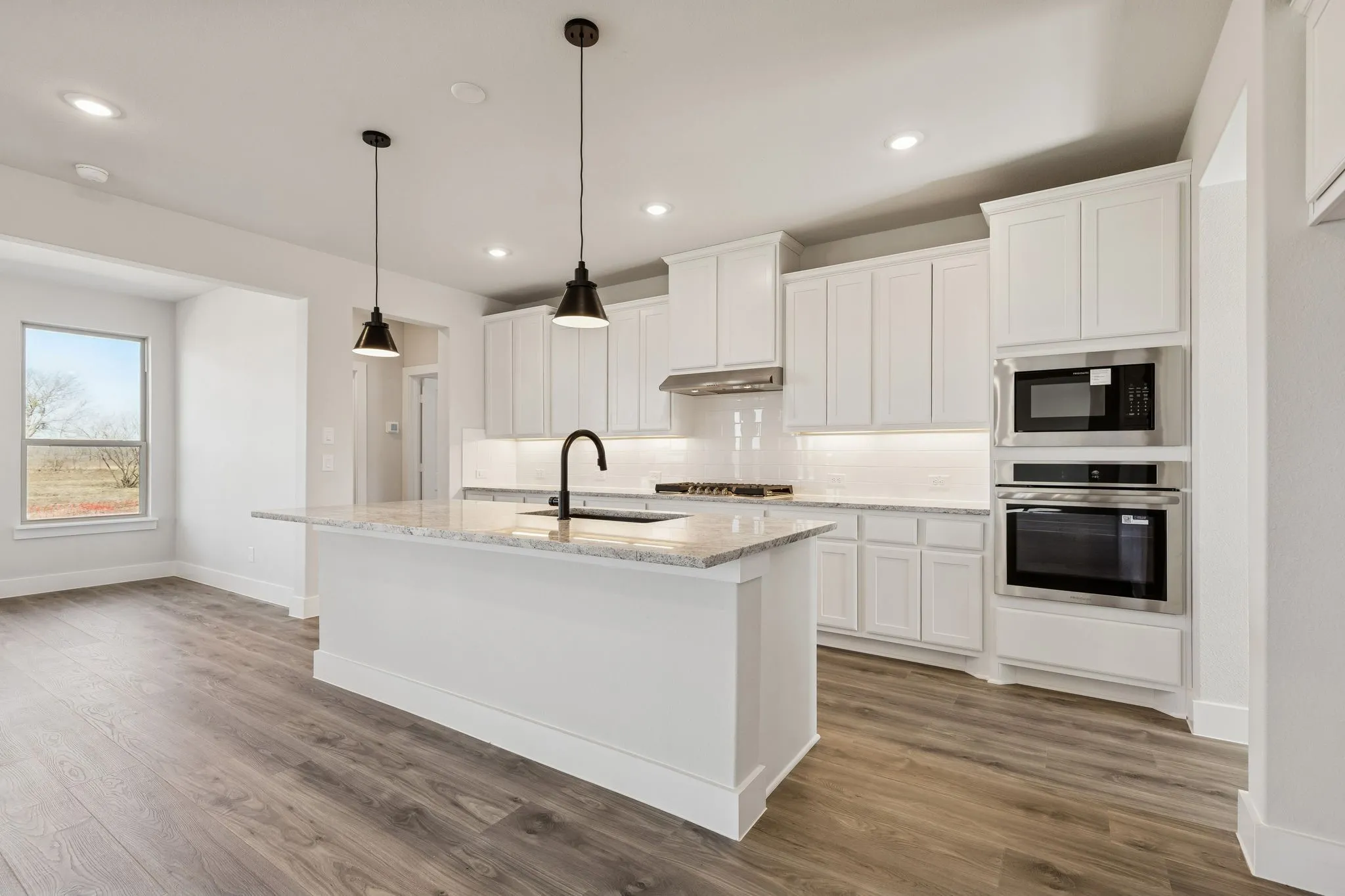 Kitchen featuring an island with stone countertop, white cabinetry, integrated stainless steel appliances, and wood-finish flooring