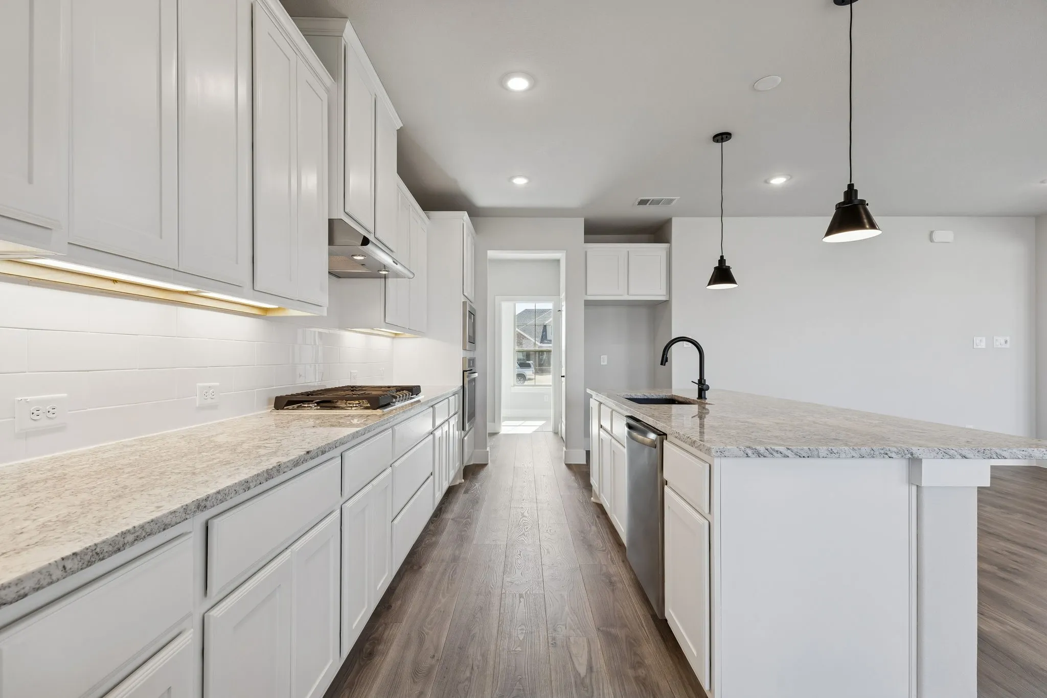 Galley kitchen featuring white shaker cabinetry, light-toned stone countertops, a full stainless steel appliance package, a built-in cooktop, and wood-finish flooring