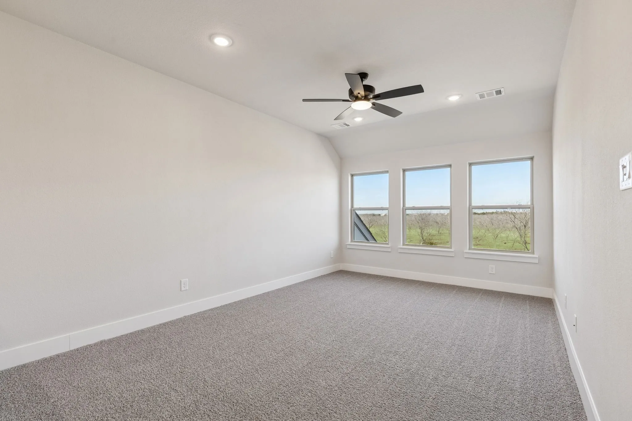 Recessed lighting, ceiling fan, three large windows, light gray carpeting, and neutral wall tones