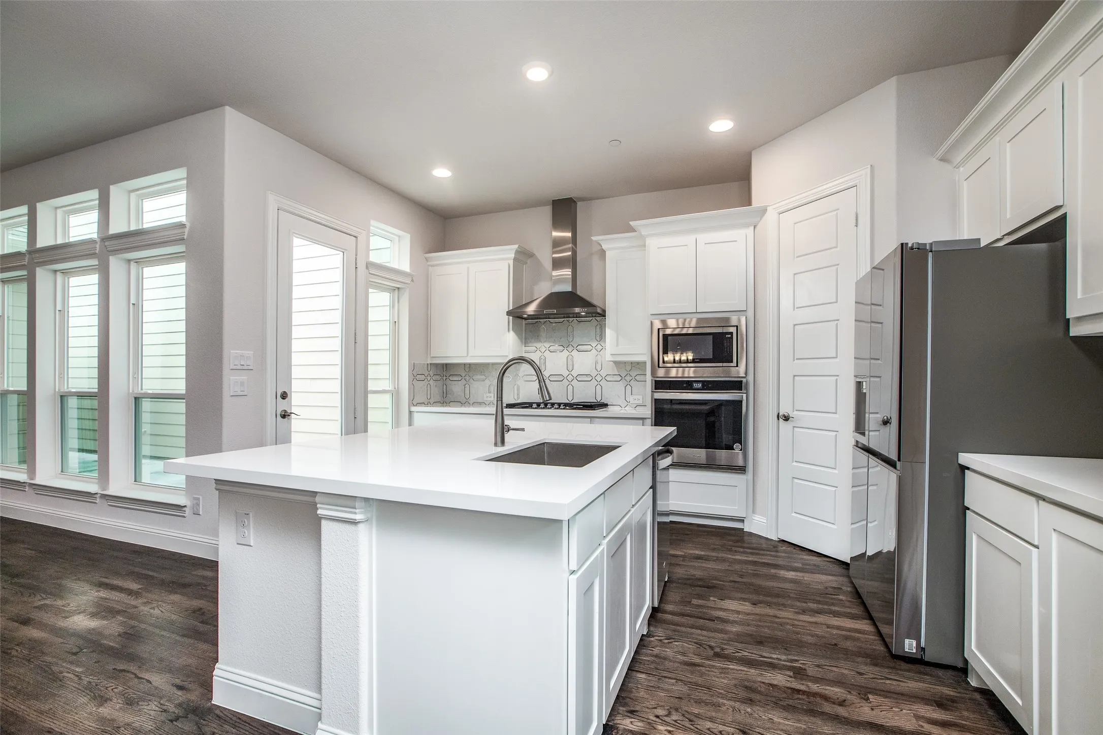 Kitchen featuring a central island with an undermount sink, white cabinetry, stainless steel appliances, and wood-finish flooring