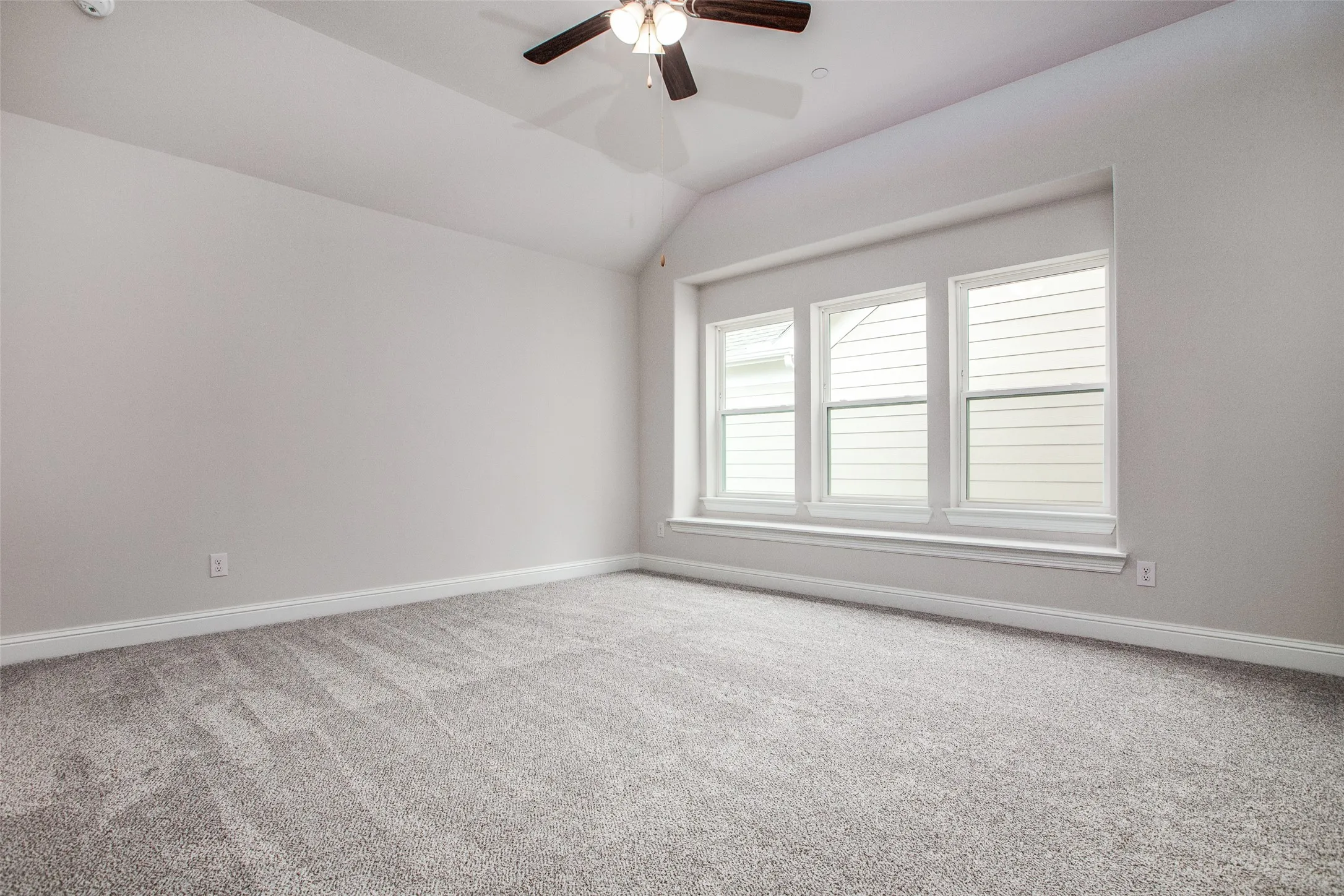 Vaulted ceiling with a ceiling fan, light-toned walls, gray-toned carpet, and a triple window