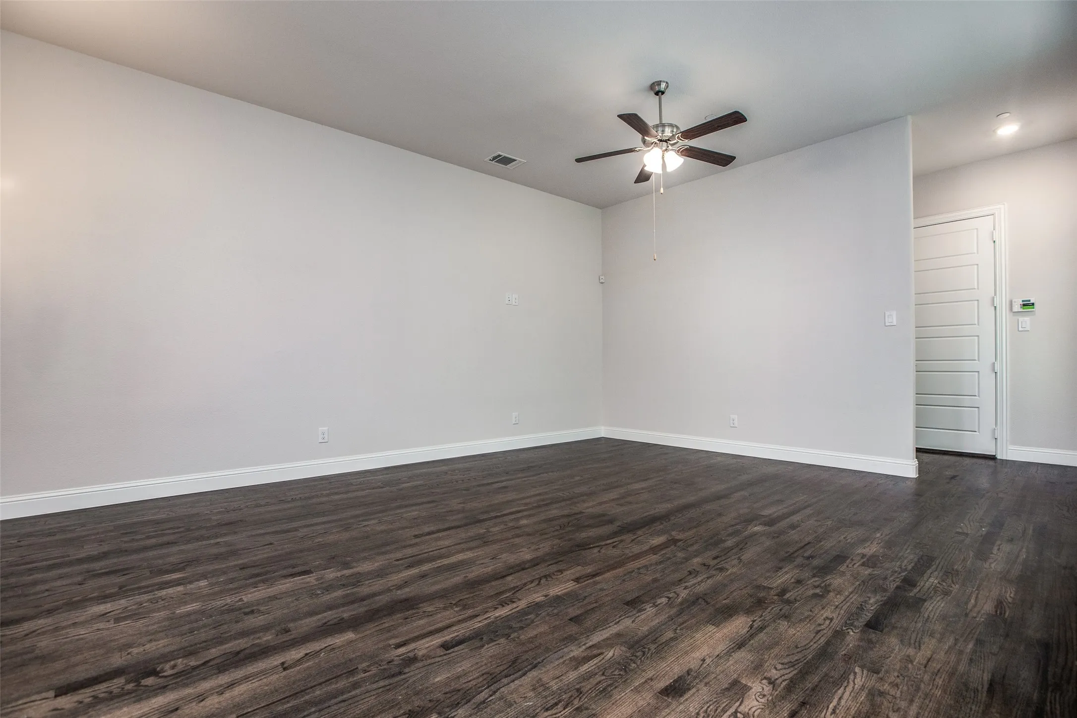 Spacious room featuring wood-finish flooring, light gray wall paint, and a ceiling fan with integrated lighting