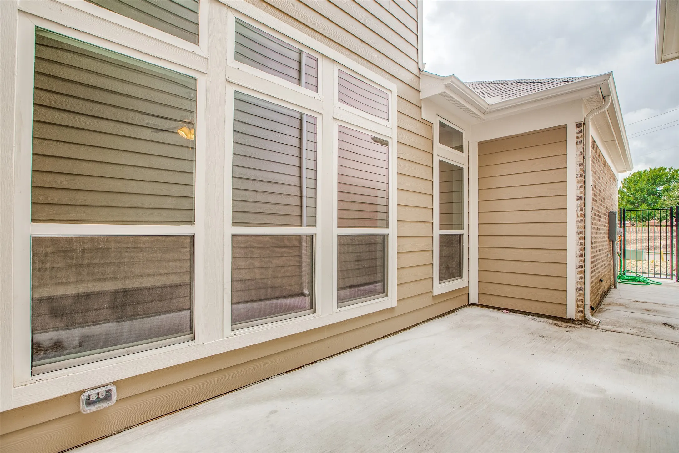 Concrete patio with exterior siding, multiple windows, and a brick accent wall