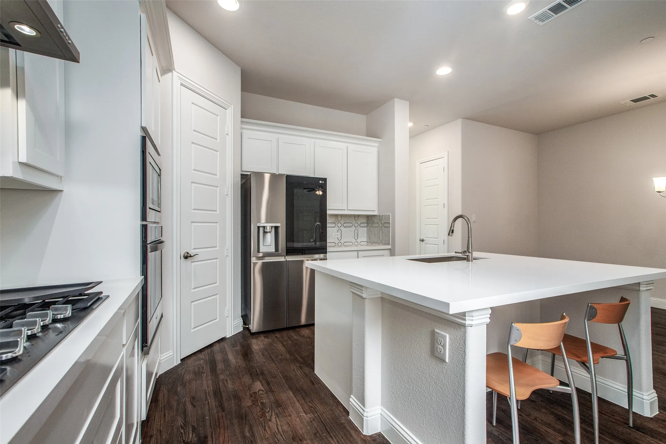 White kitchen cabinetry, stainless steel appliances, solid surface countertops, wood-finish flooring, and recessed lighting