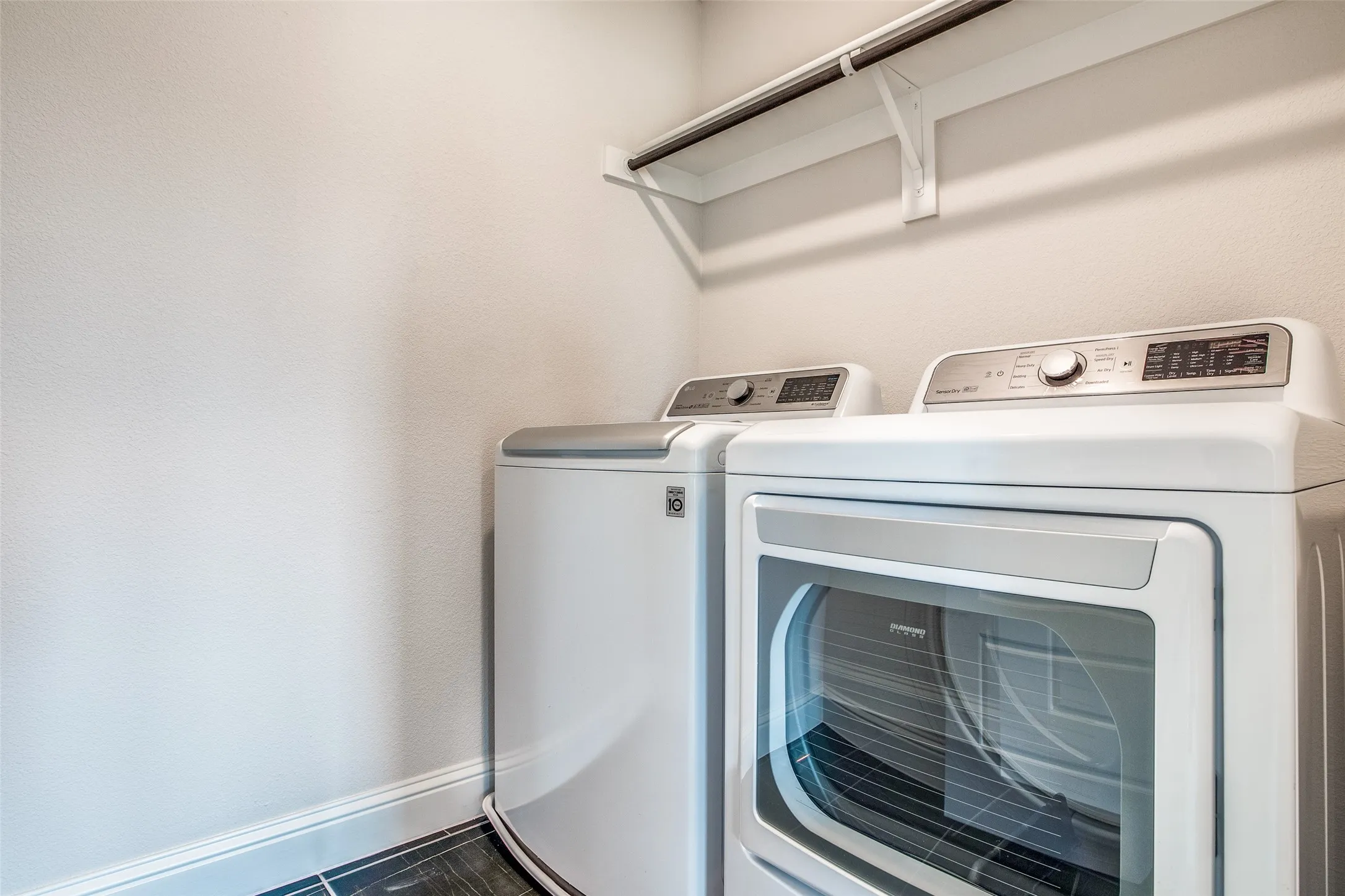 Laundry area featuring a hanging rod and dark tile flooring