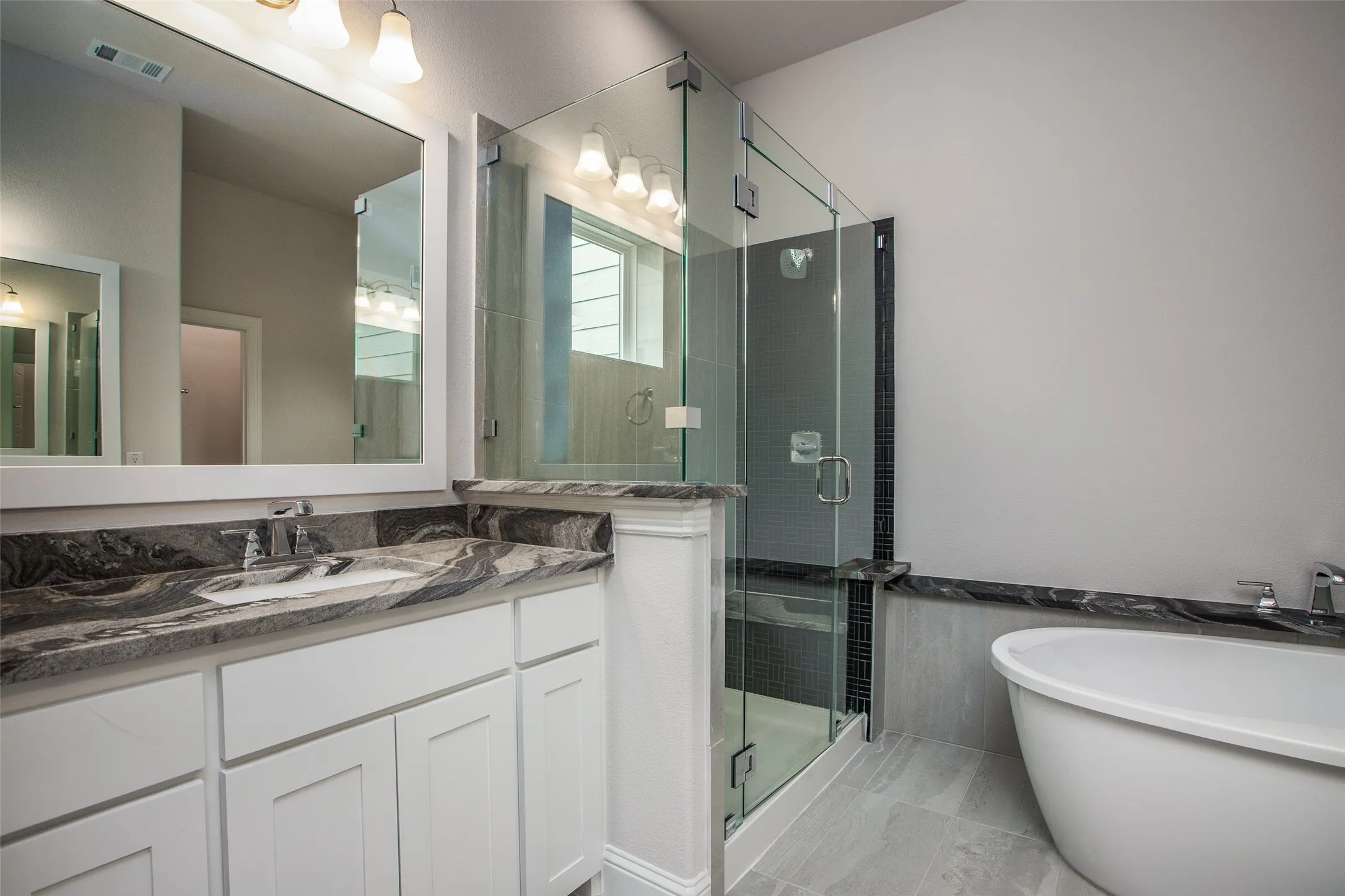 Spacious bathroom featuring a freestanding tub, glass-enclosed shower, dual vanity with undermount sinks, and stone countertops