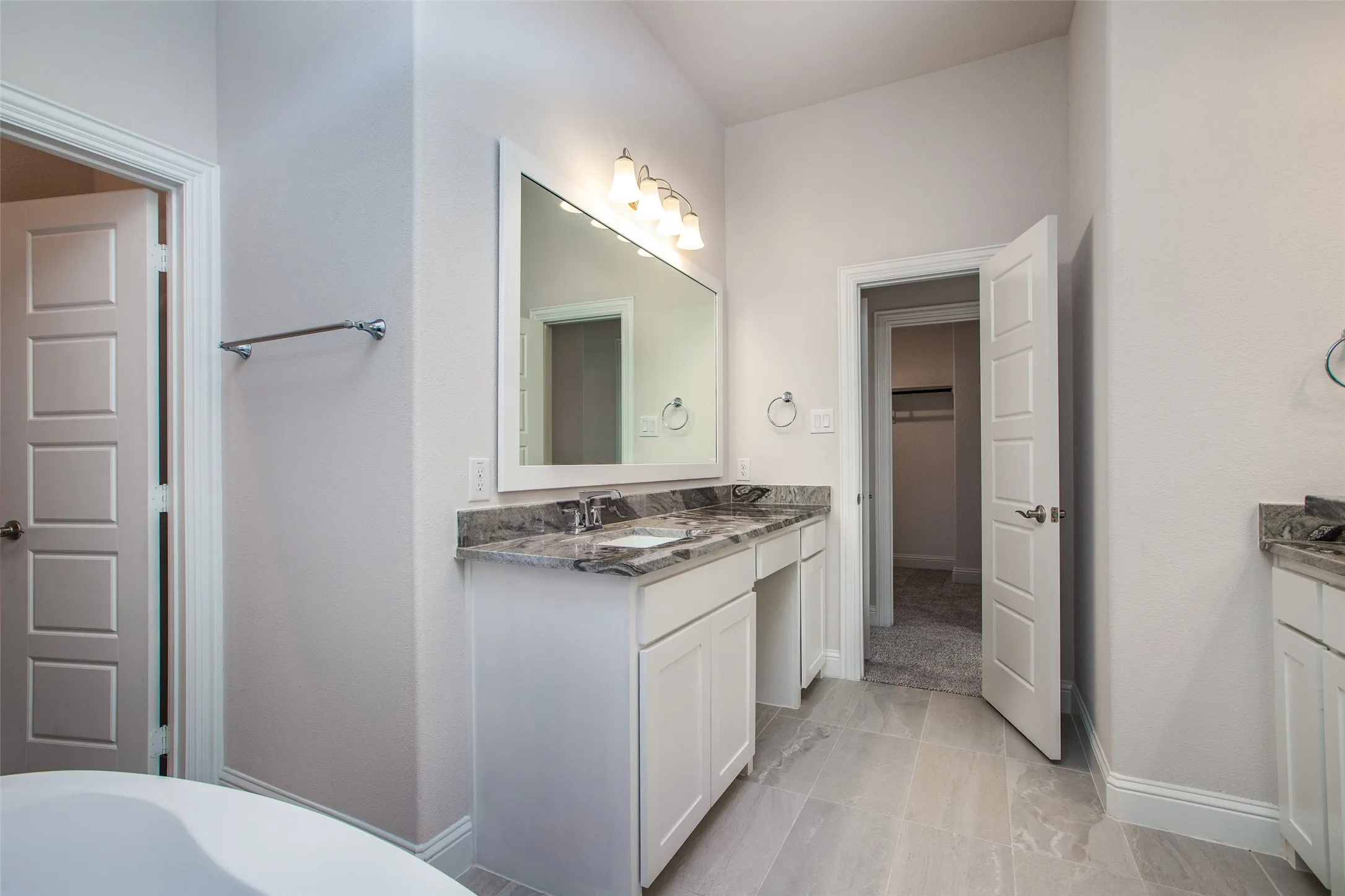 Dual vanity with stone countertops, white cabinetry, and a framed mirror with integrated lighting