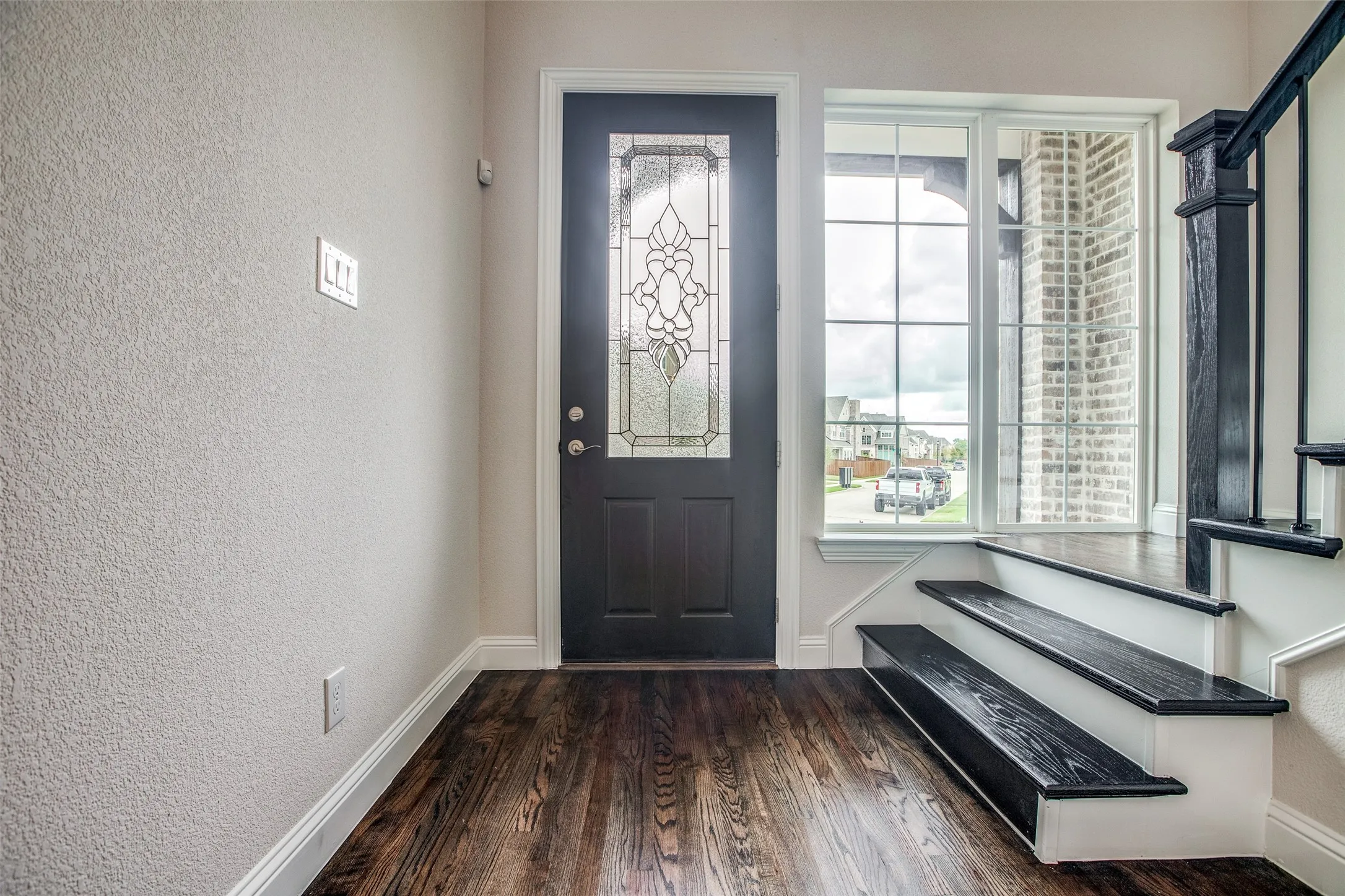 Dark wood-finish flooring, entry door with decorative glass inlay, and a multi-pane window