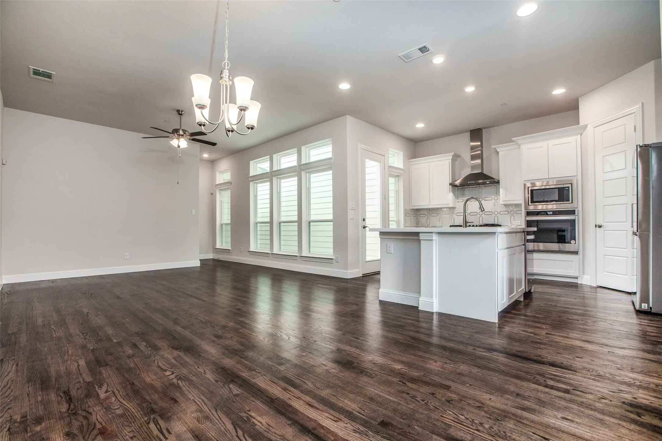 Dark wood-finish flooring throughout, white cabinetry, stainless steel appliances, a kitchen island, and multiple large windows