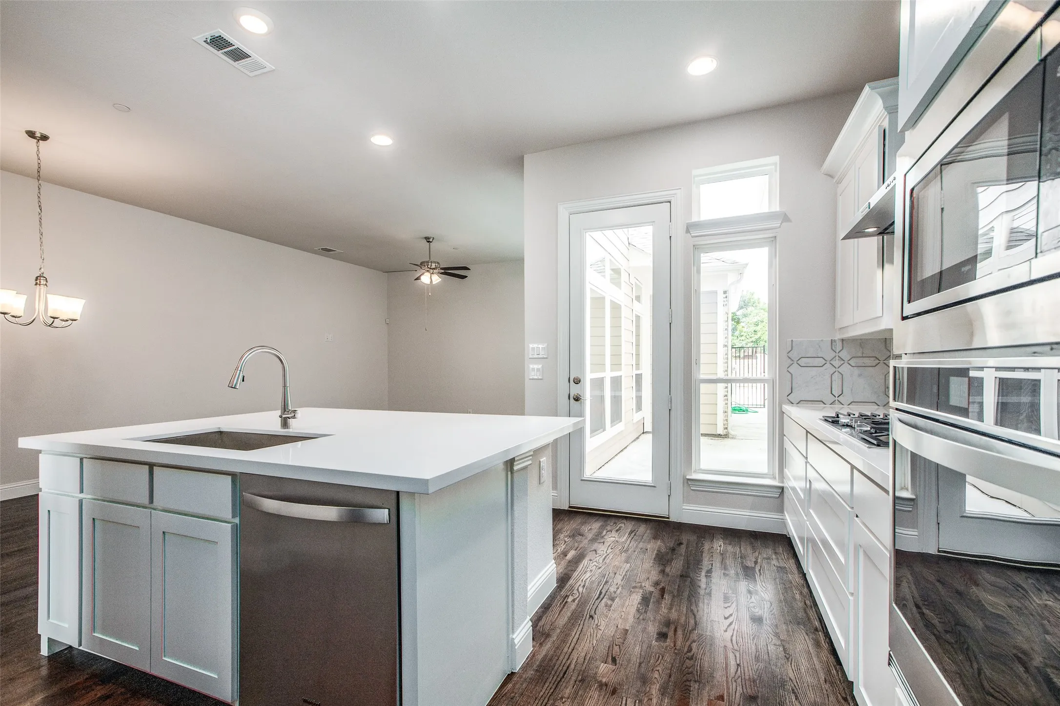 Kitchen featuring a center island with sink, stainless steel appliances, white cabinetry, and wood-finish flooring