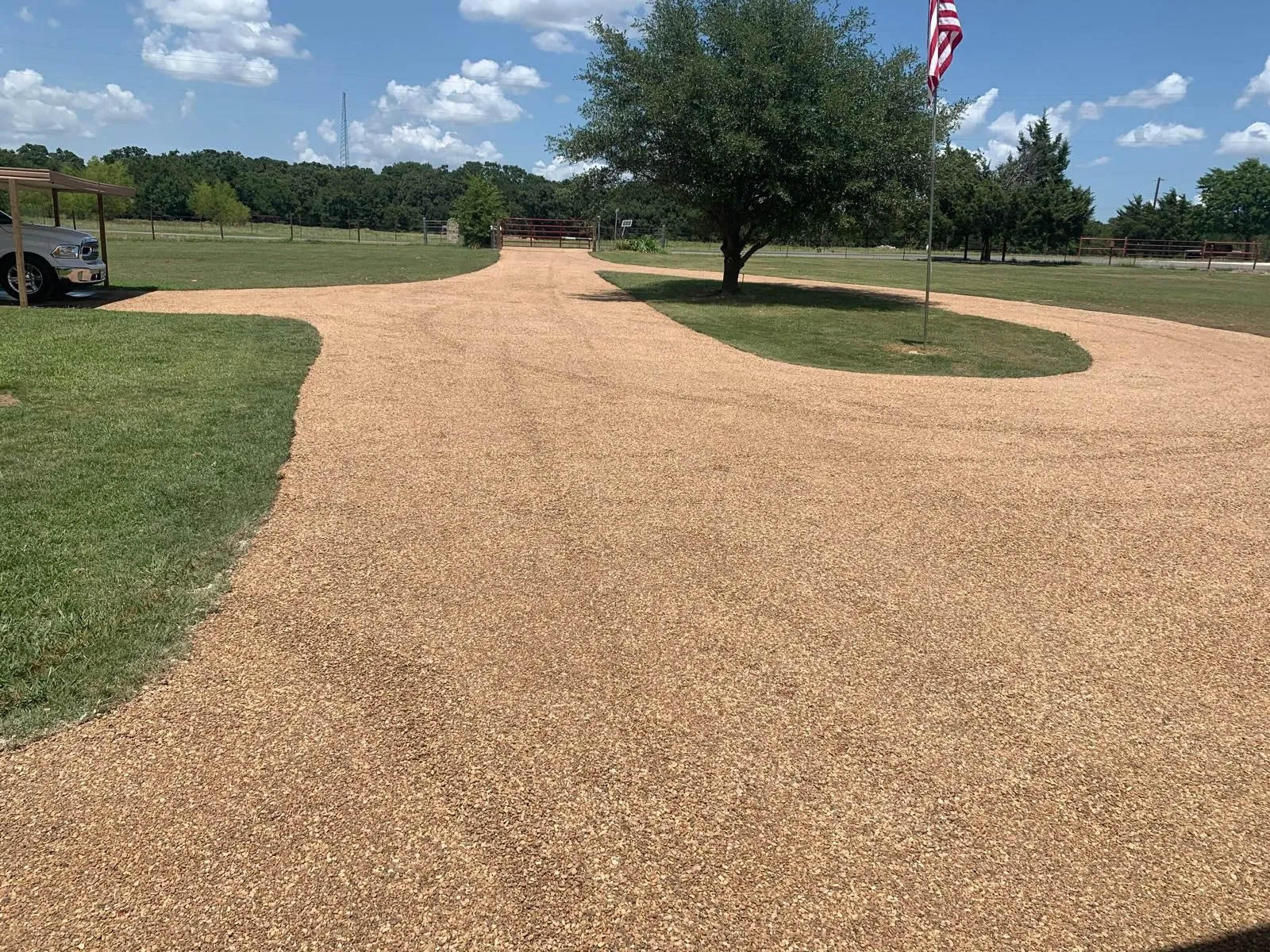 Expansive gravel driveway with a circular turnaround, manicured lawn, mature trees, and a covered carport