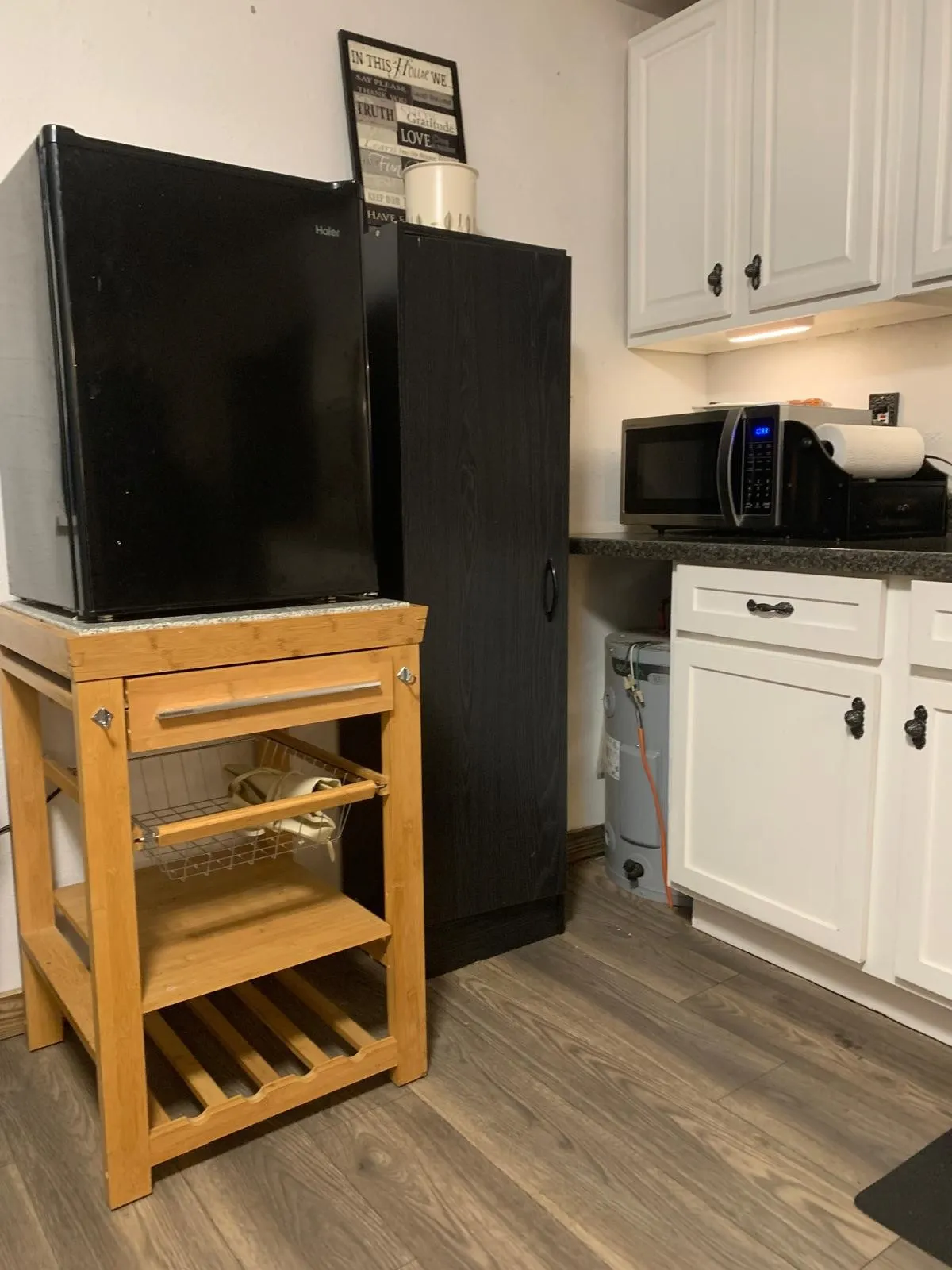 White upper and lower cabinetry with dark hardware, dark countertops, and wood-finish flooring