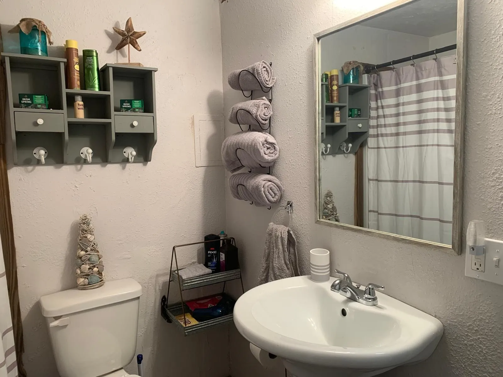 Wall-mounted sink with chrome faucet, a rectangular mirror, and a wall-mounted storage shelf with hooks