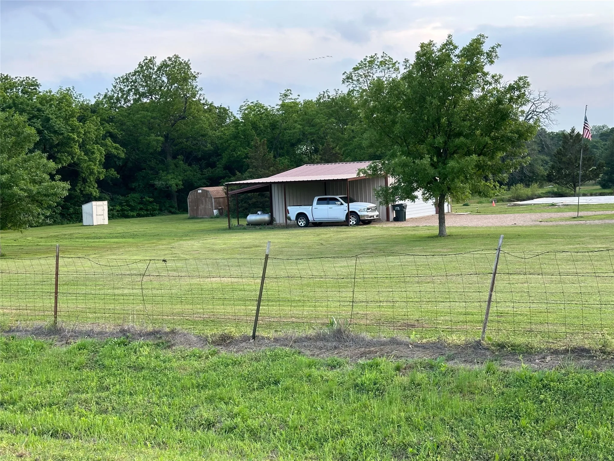 Expansive green space with mature trees, a metal-roofed carport, and a storage shed