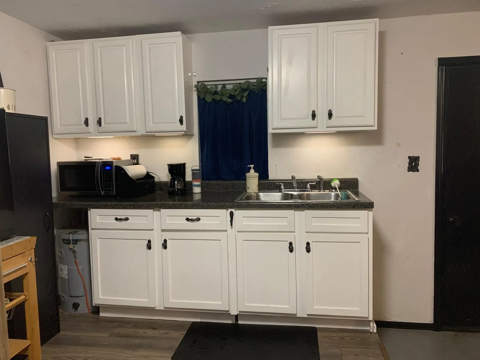 White shaker-style cabinetry with dark hardware, dark countertop, stainless steel double basin sink, and wood-finish flooring