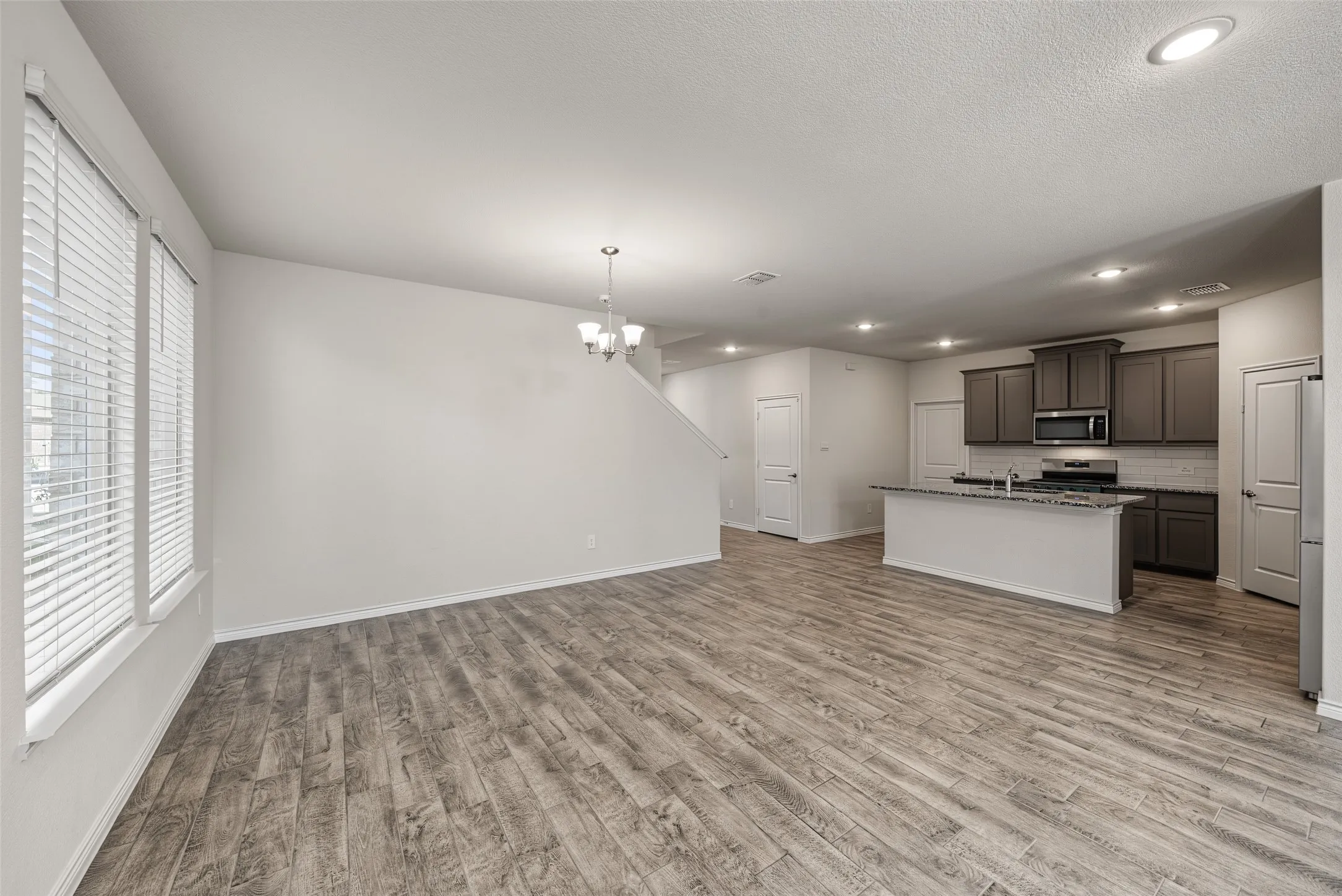 Open-concept living area featuring porcelain tile flooring, recessed lighting, and a modern kitchen with gray cabinetry, stainless steel appliances, and a central island with a breakfast bar