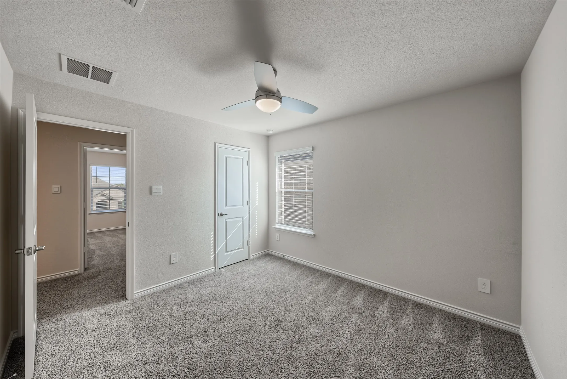 Plush gray carpeting, white trim work, ceiling fan with integrated lighting, and window with blinds