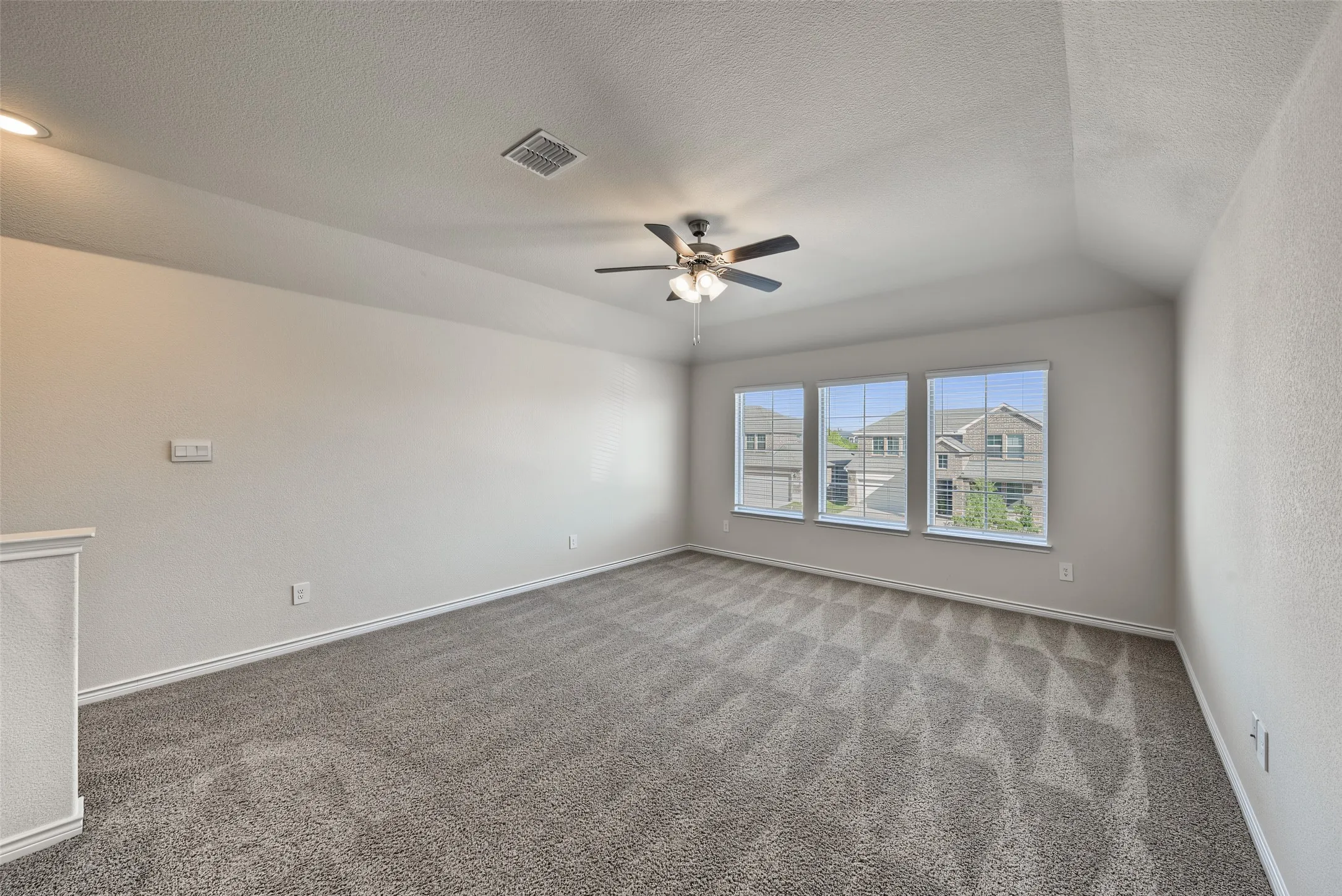 Spacious room featuring vaulted ceilings, a ceiling fan with integrated lighting, three windows with horizontal blinds, and carpet flooring