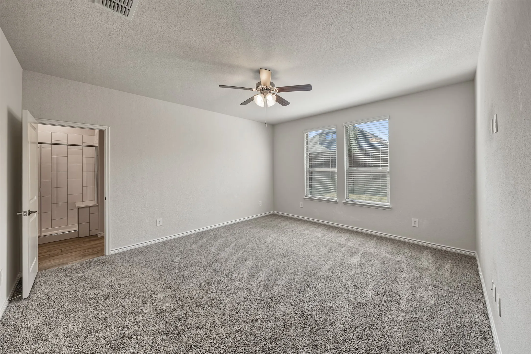 Carpeted flooring, ceiling fan with light fixture, two windows with blinds, and white interior walls