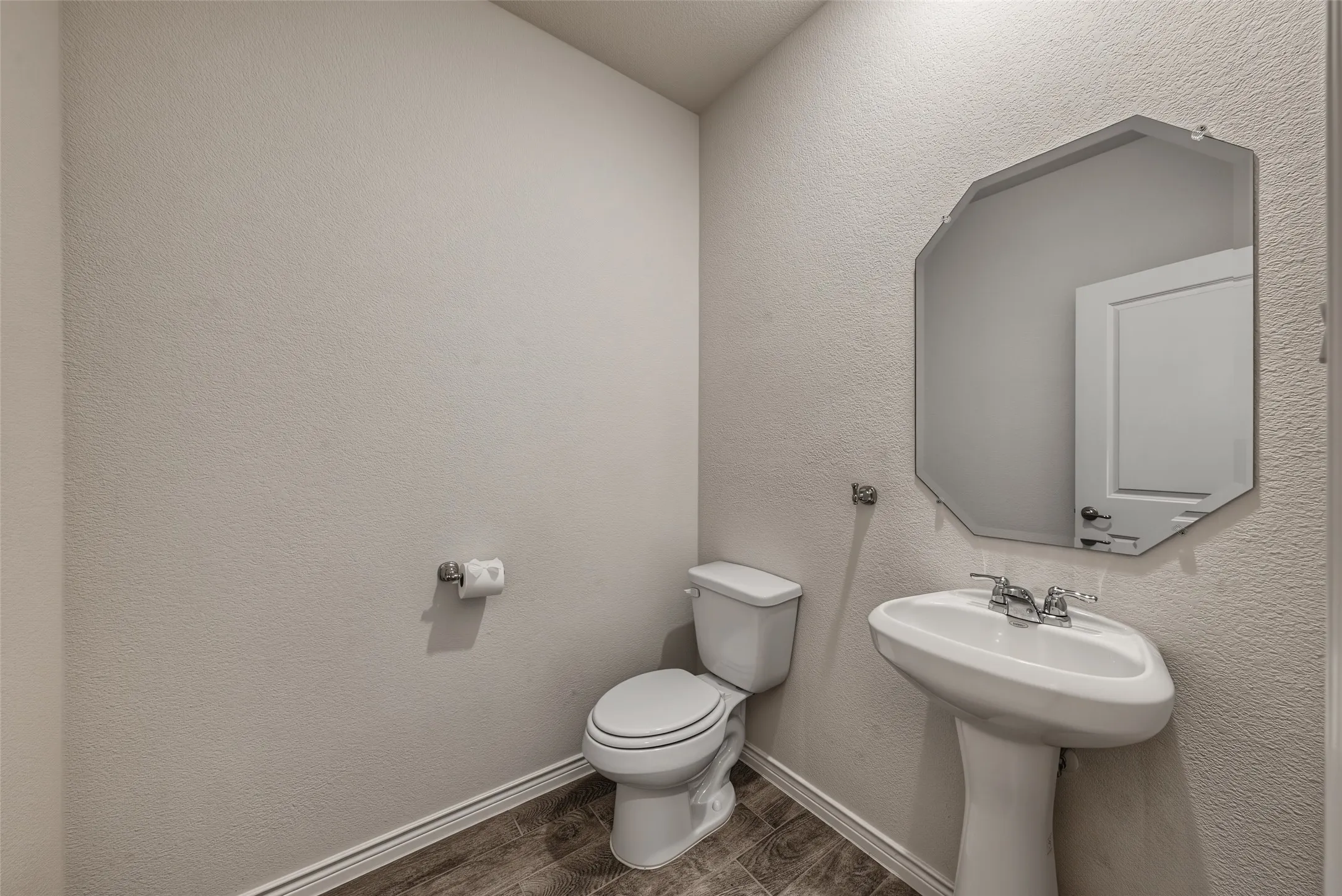 Downstairs 1/2 bath with pedestal sink w/ chrome faucet, octagonal wall mirror, and porcelain tile flooring