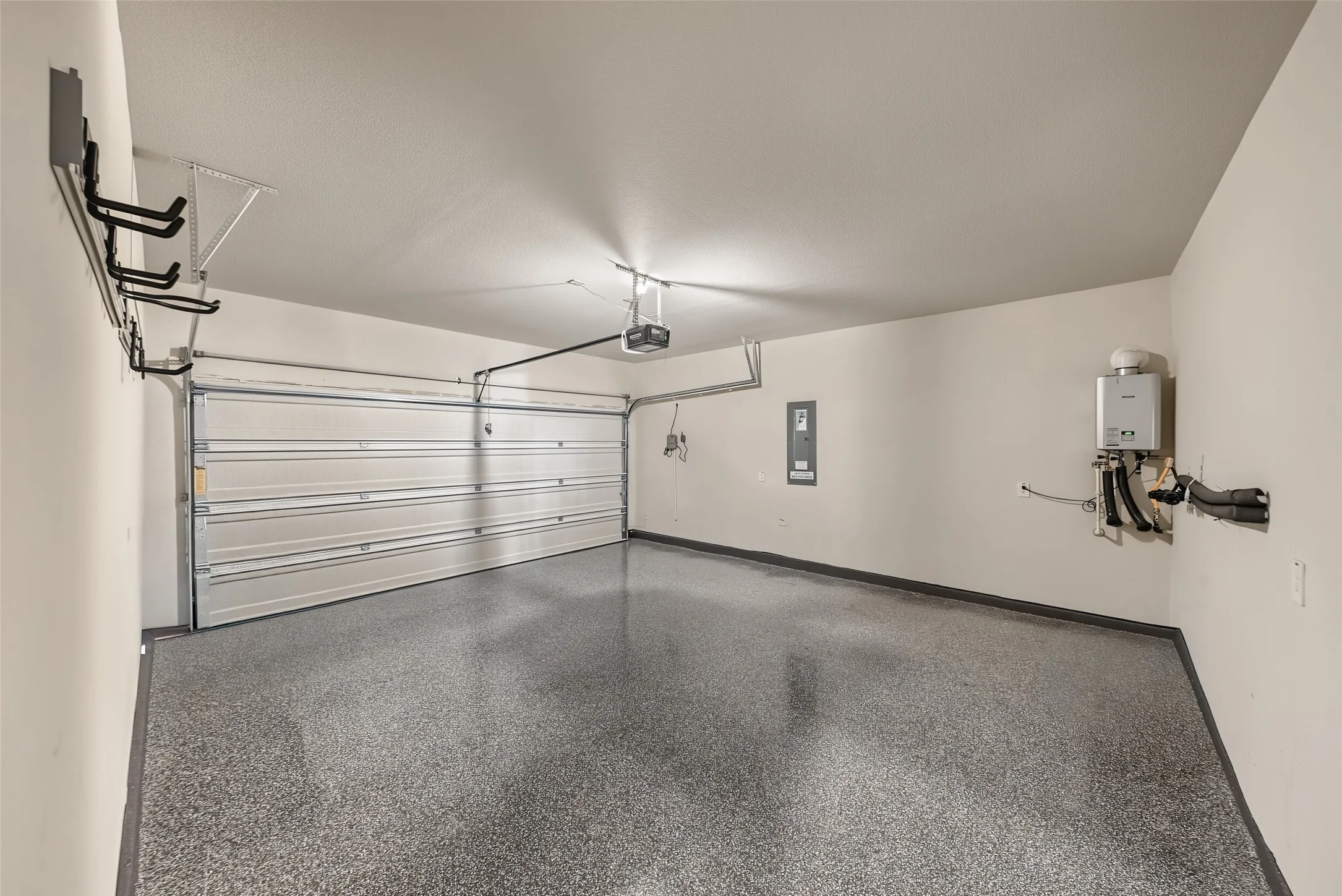Garage with speckled epoxy flooring, overhead door opener, wall-mounted storage racks, and a tankless water heater