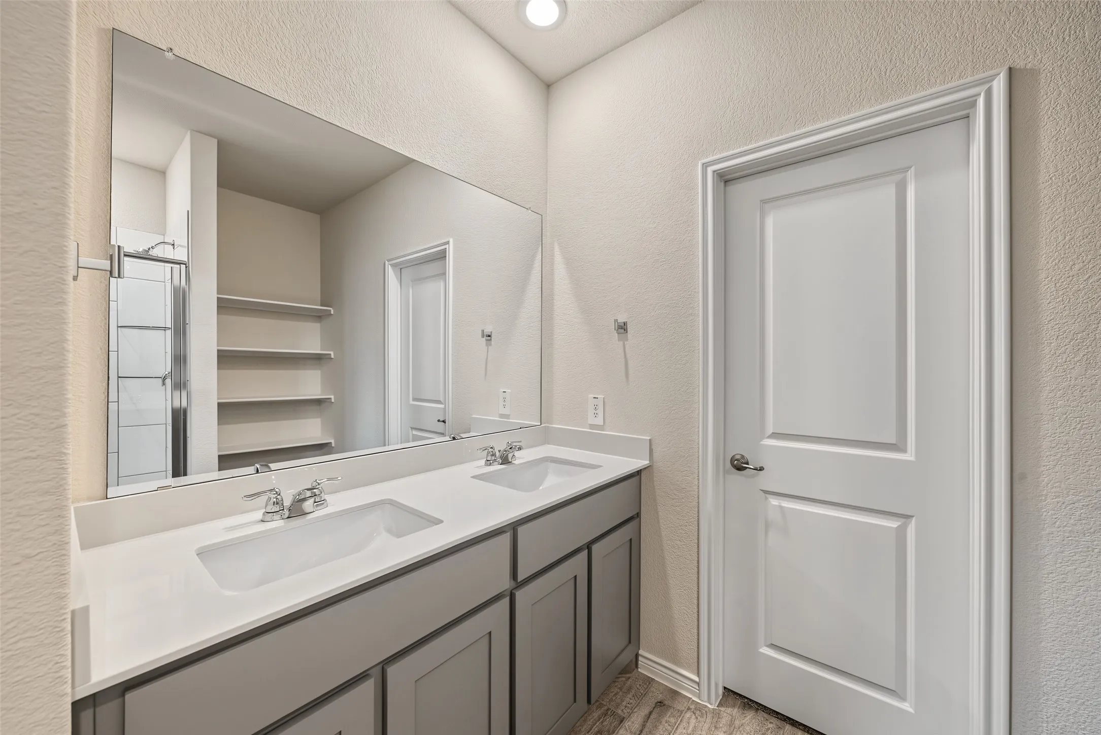 Dual vanity with undermount sinks, chrome fixtures, a large frameless mirror, and wood-finish flooring