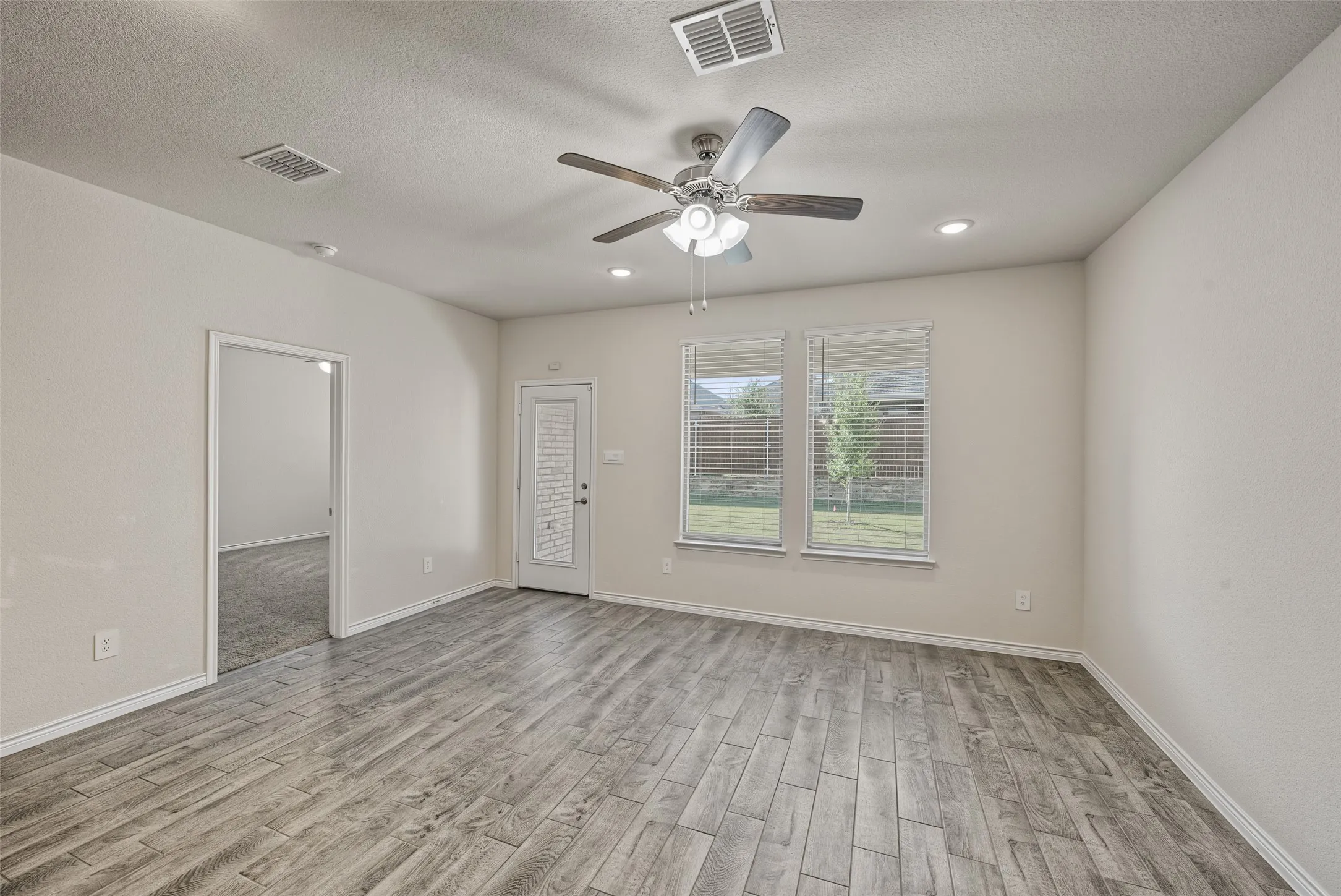 Wood-finish flooring, multiple windows with blinds, recessed lighting, ceiling fan, and a door with an integrated window