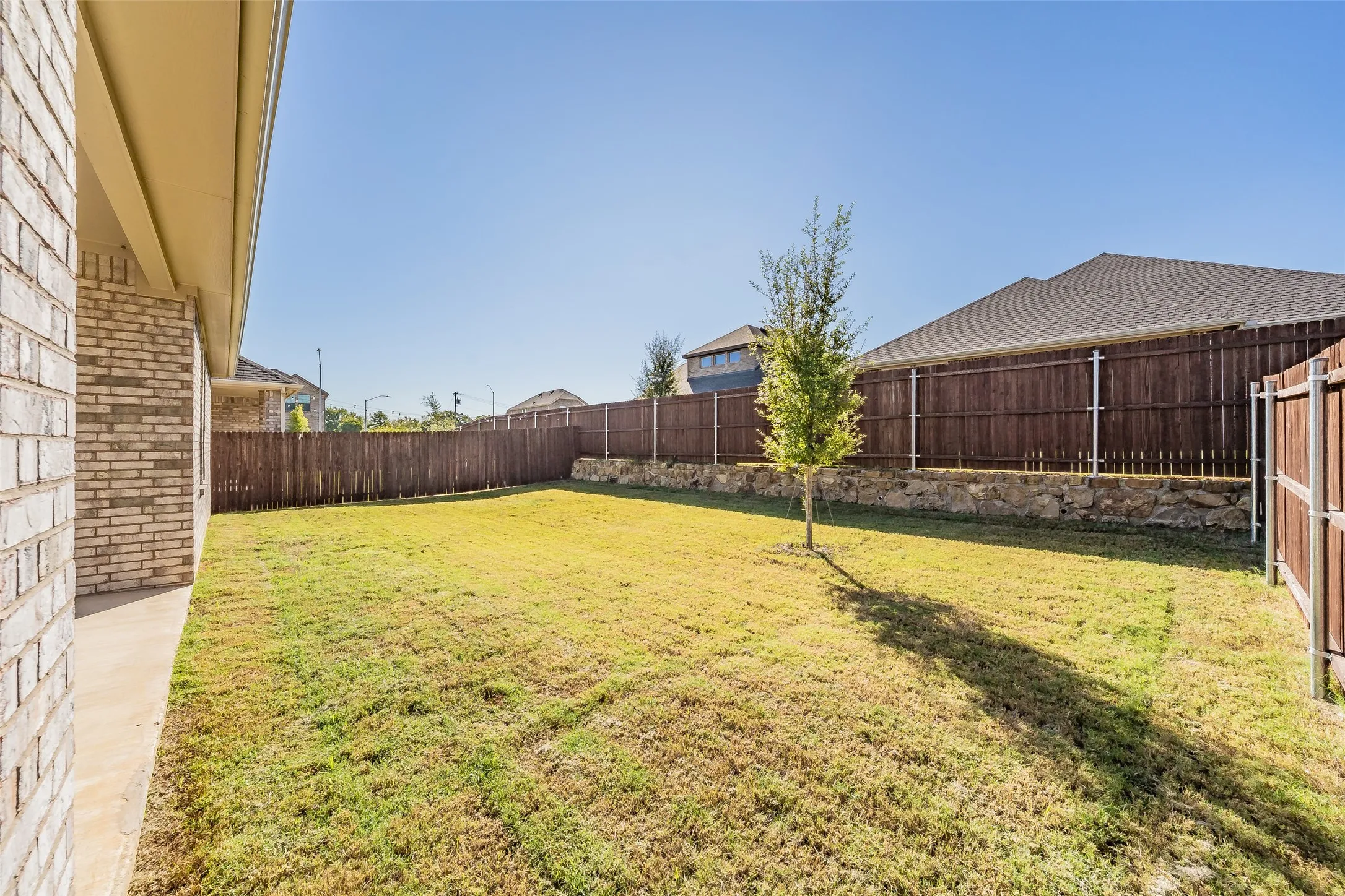 Expansive backyard featuring a manicured lawn, established tree, and a natural stone retaining wall