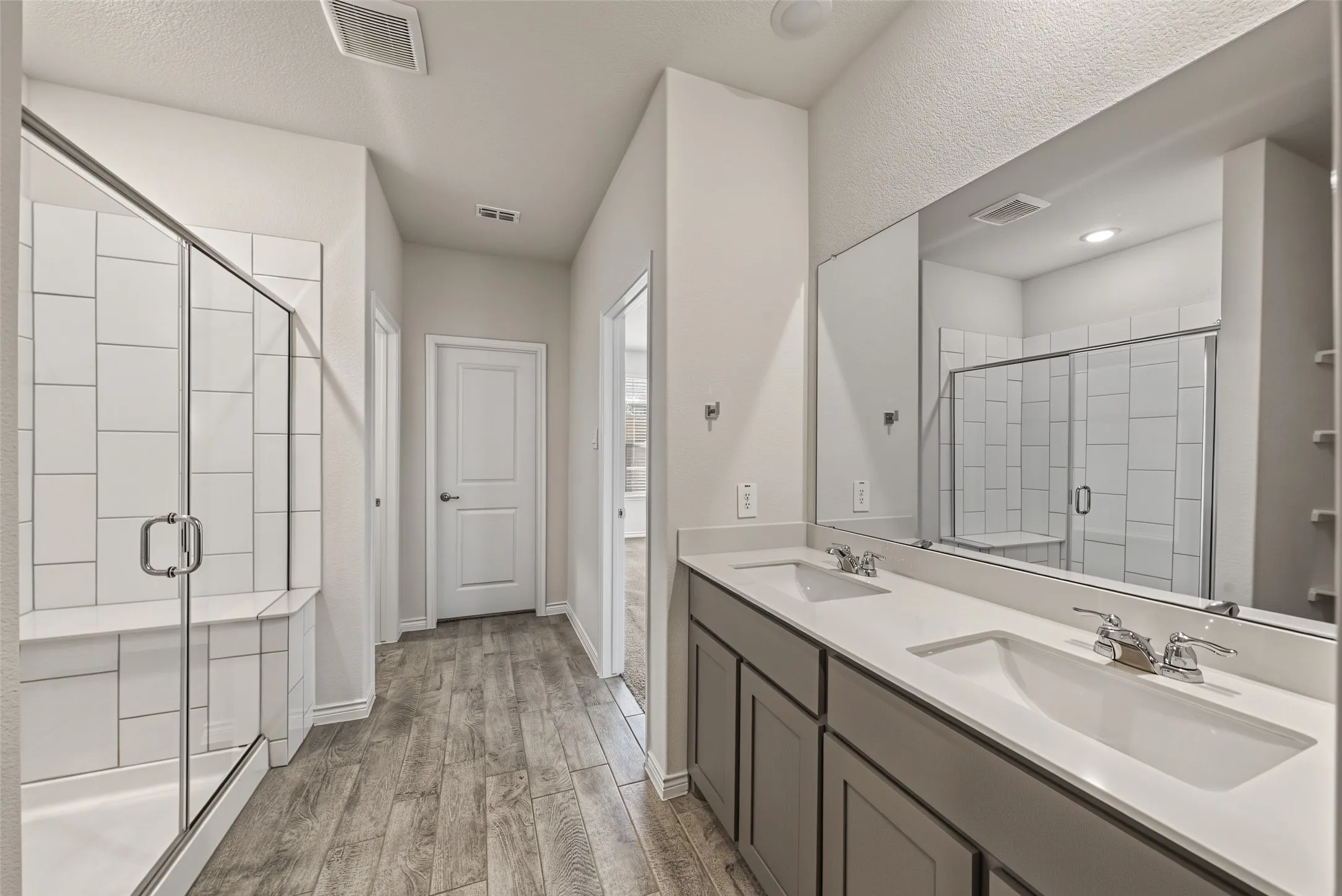Dual vanity with integrated sinks, porcelain tile flooring, glass-enclosed shower with tiled walls and built-in bench, and a large wall-mounted mirror