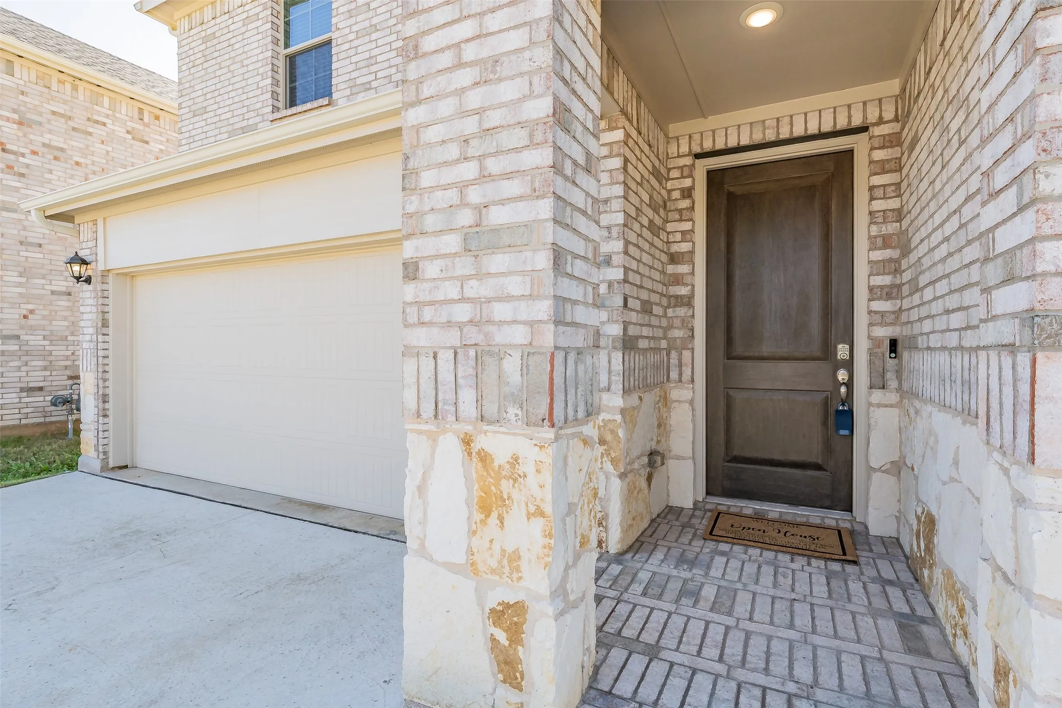 Brick and stone veneer exterior with an attached garage, featuring a recessed entry with a wood-panel front door and a brick paver porch
