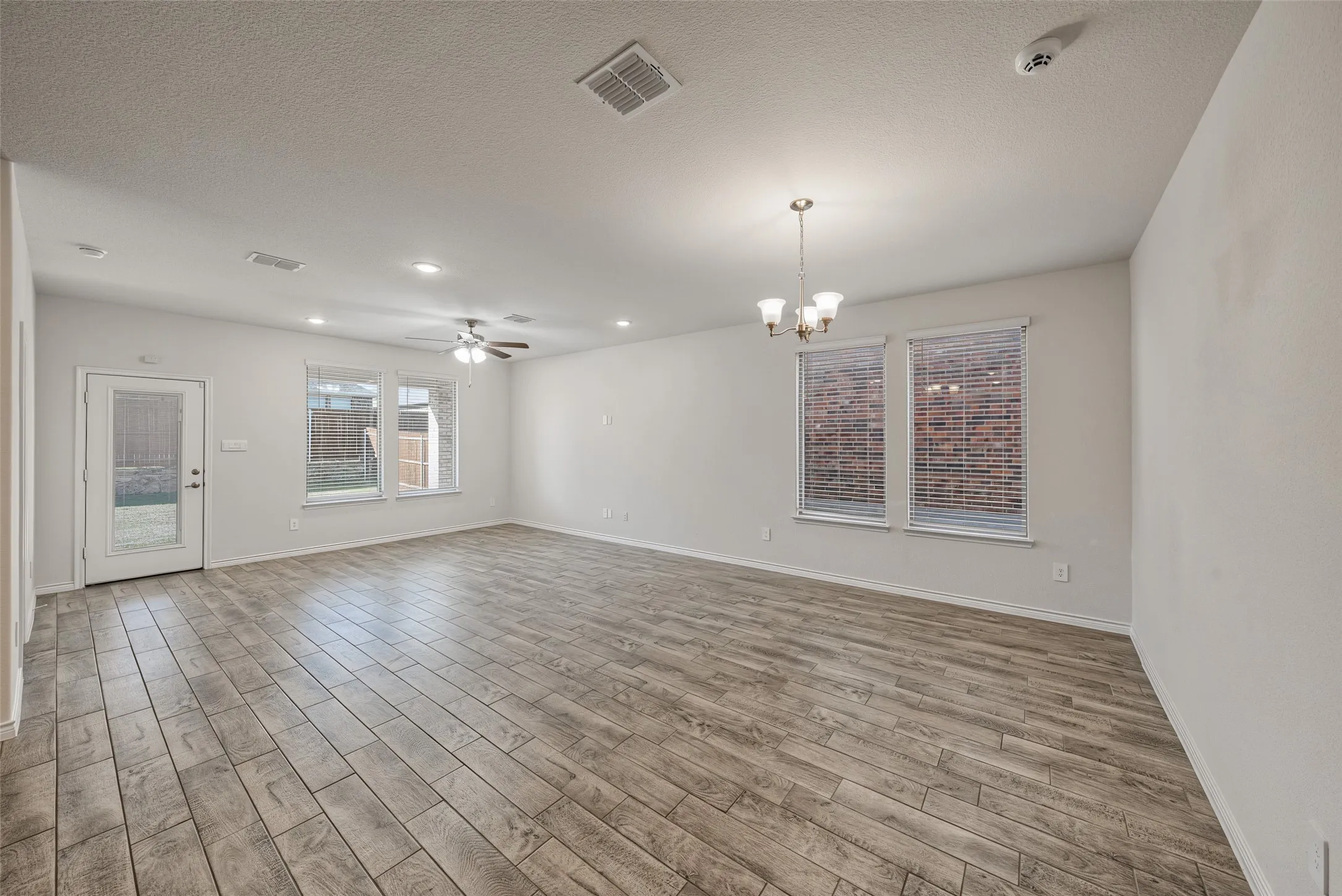 Spacious open-concept living area featuring porcelain tile flooring throughout, recessed lighting, ceiling fan, and large windows framed with brick exterior views