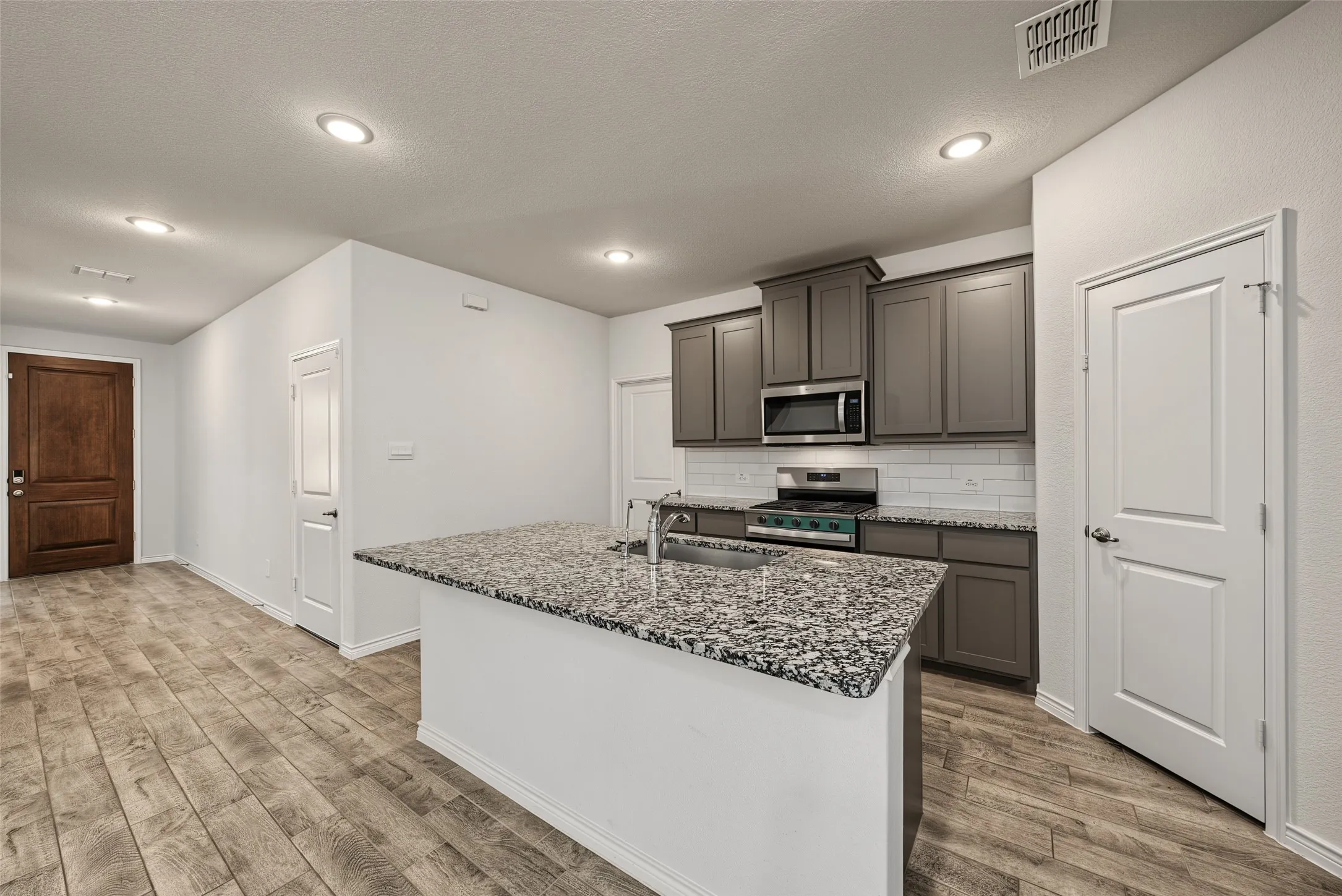 Kitchen featuring gray cabinetry, stainless steel appliances, a white subway tile backsplash, and a large island with a speckled granite countertop