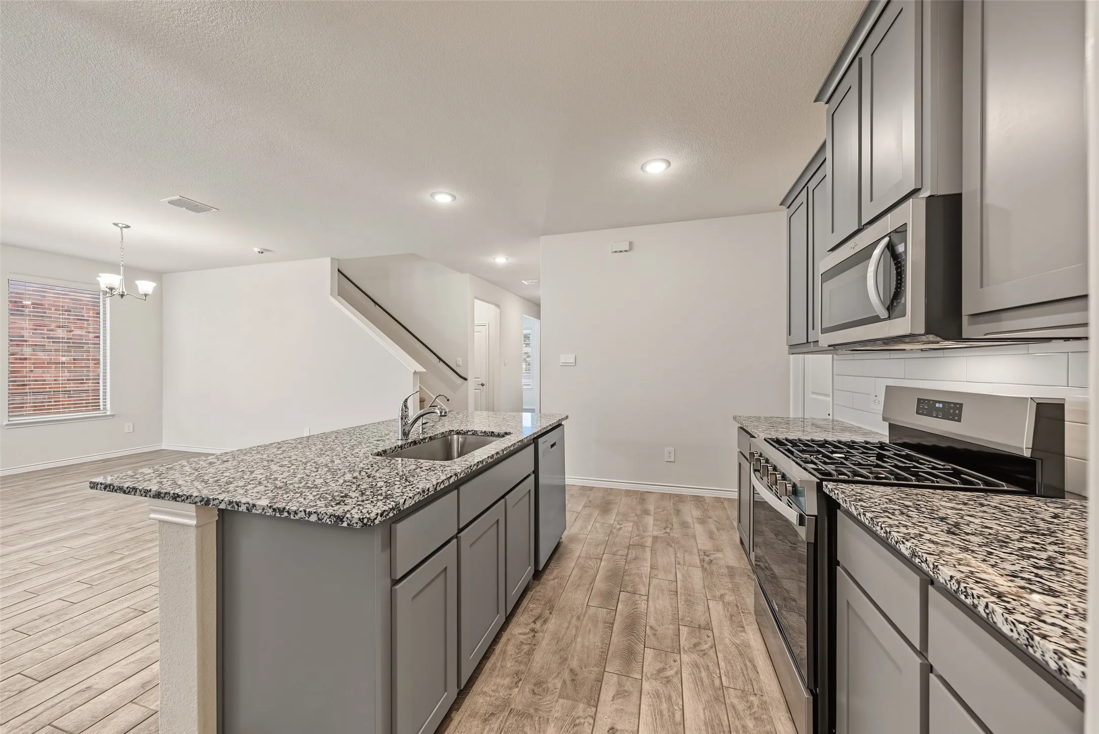 Kitchen featuring grey shaker-style cabinetry, stainless steel appliances, granite countertops, and a subway tile backsplash