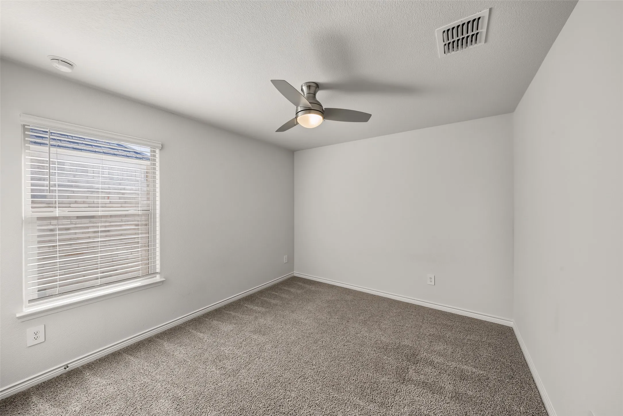 Neutral wall color, carpeted flooring, window with blinds, and a ceiling fan with integrated lighting