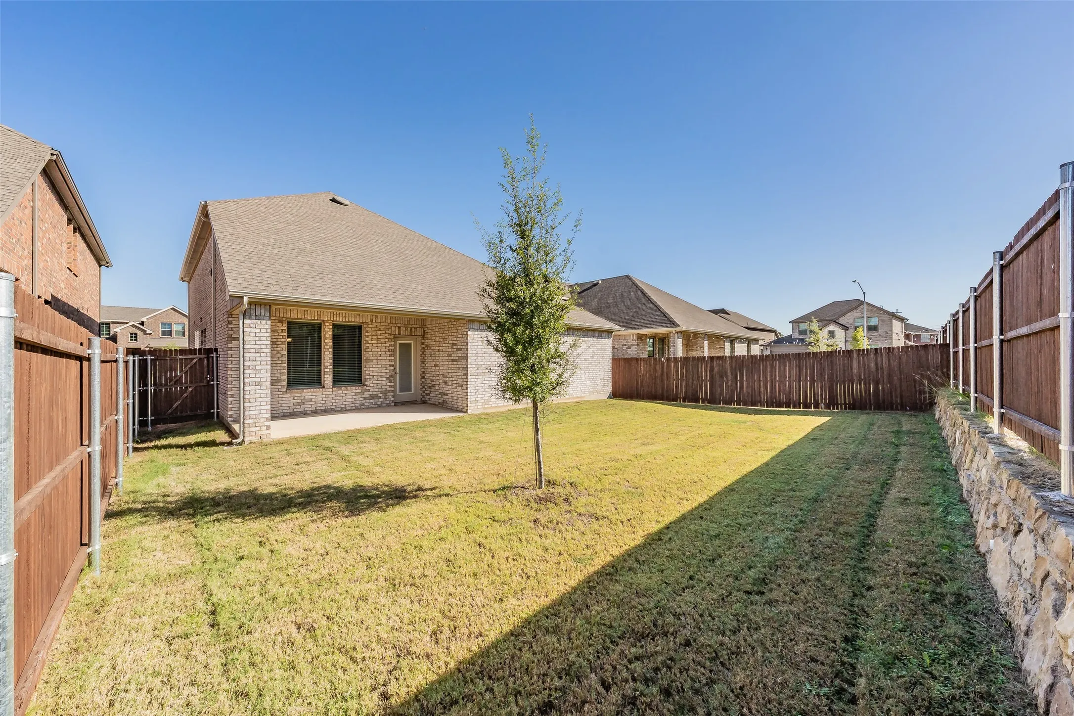 Expansive backyard featuring a manicured lawn, full privacy fencing, and a stone retaining wall