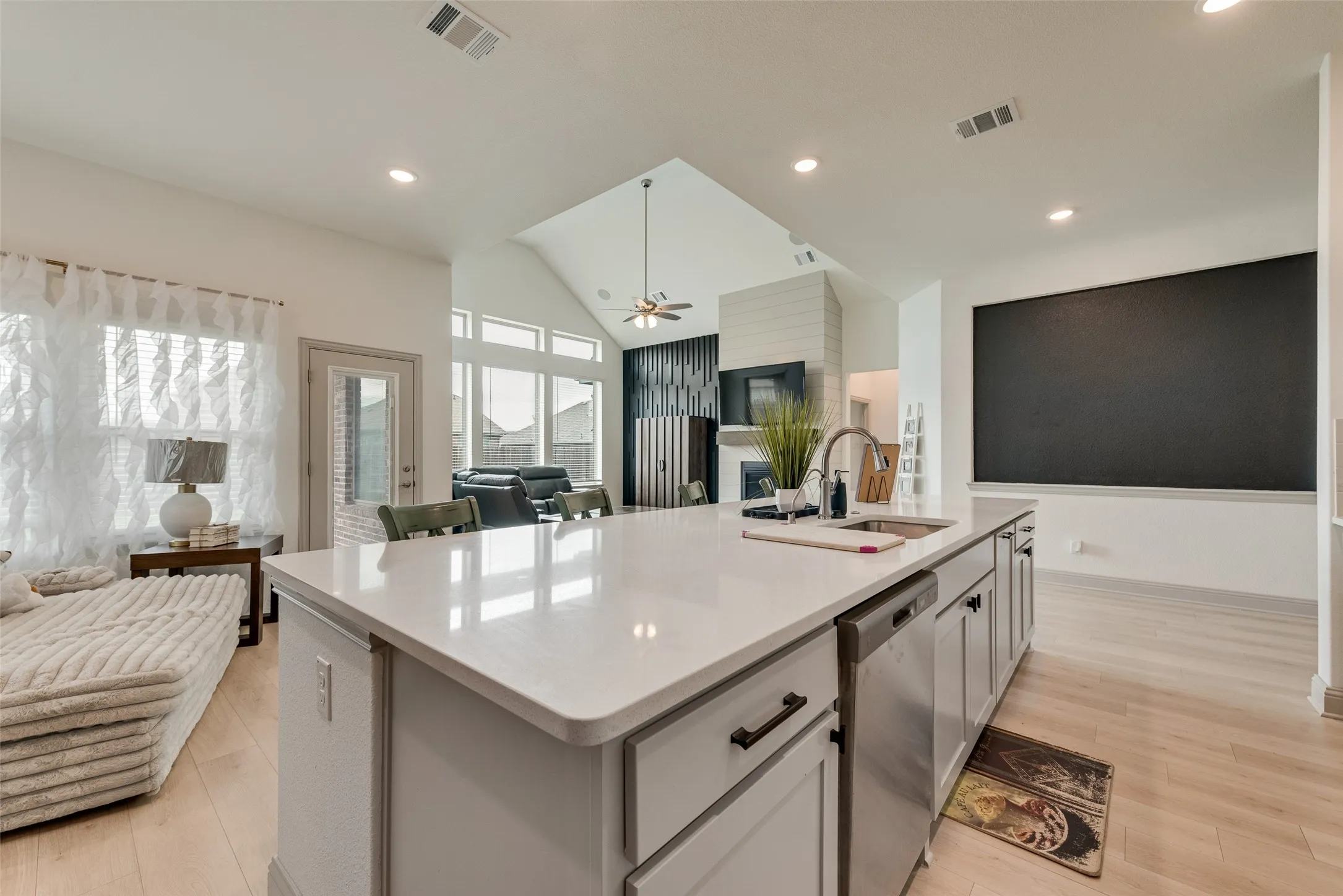 Kitchen island with a stainless steel sink, pull-down faucet, integrated dishwasher, and light-toned countertops